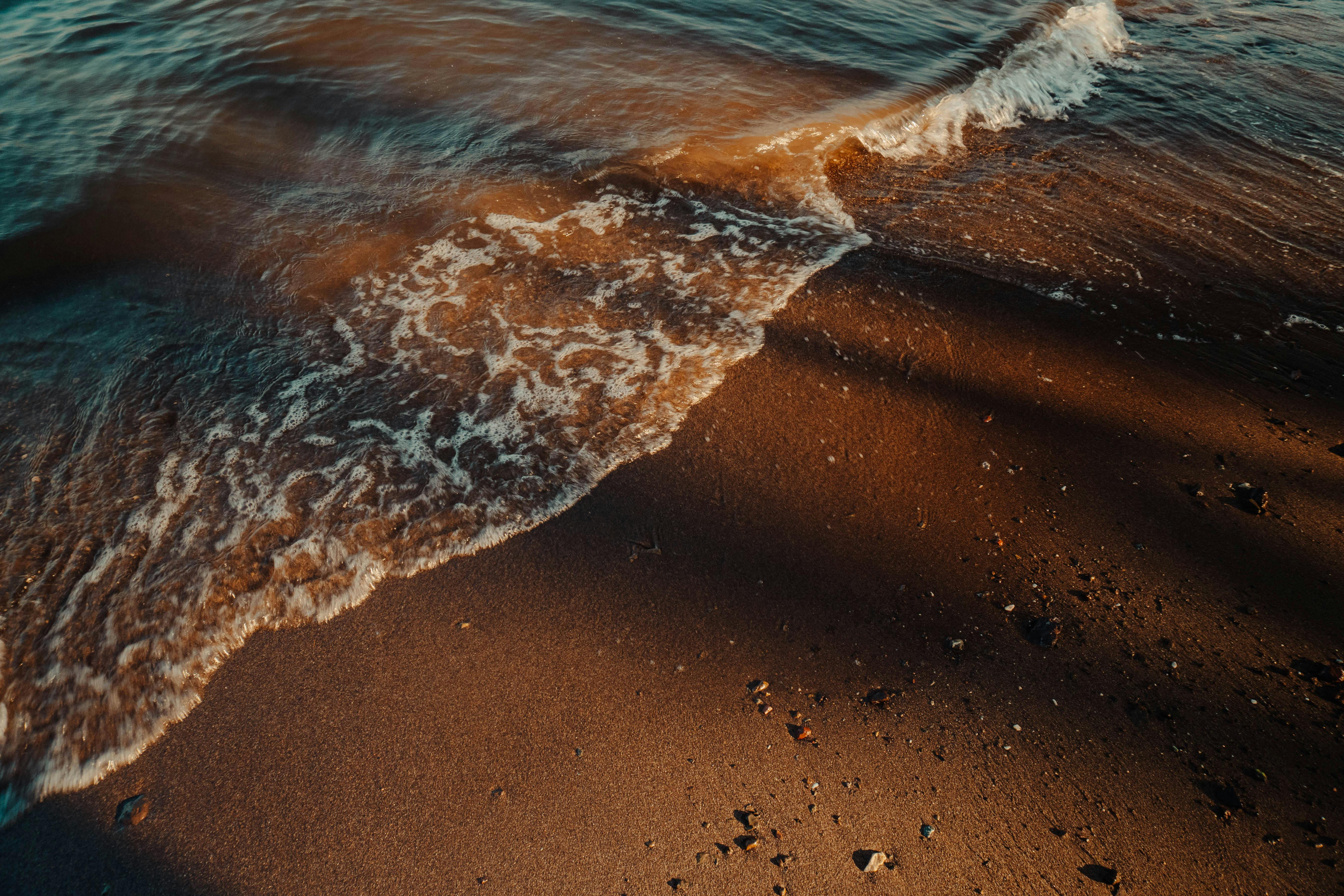 Free Gentle waves wash over a sandy beach at sunset, creating a calming seaside scene. Stock Photo