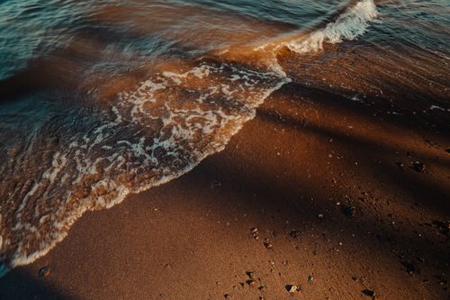 Free Gentle waves wash over a sandy beach at sunset, creating a calming seaside scene. Stock Photo