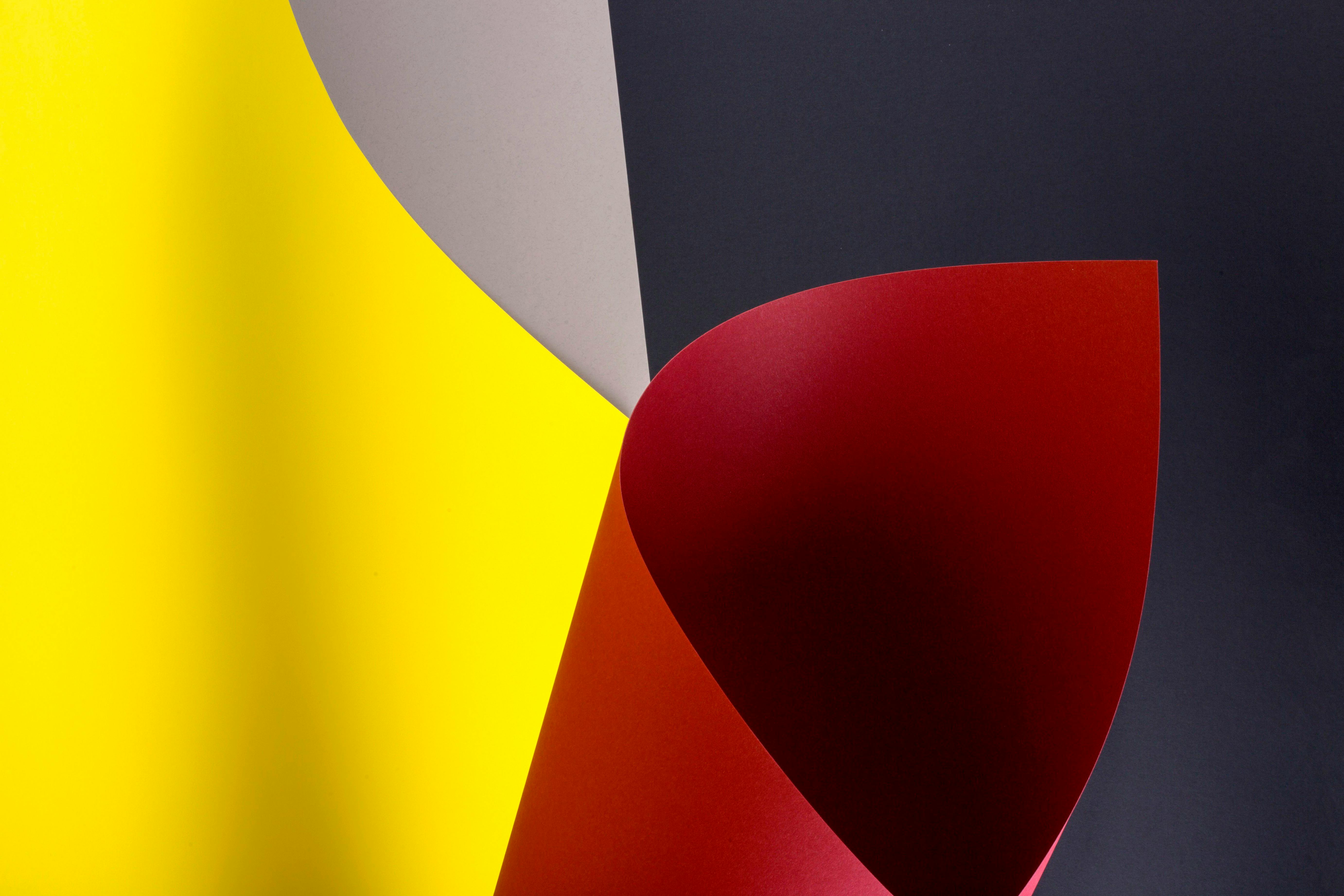 Free Vibrant abstract image featuring curved sheets of yellow, red, gray, and dark paper. Stock Photo