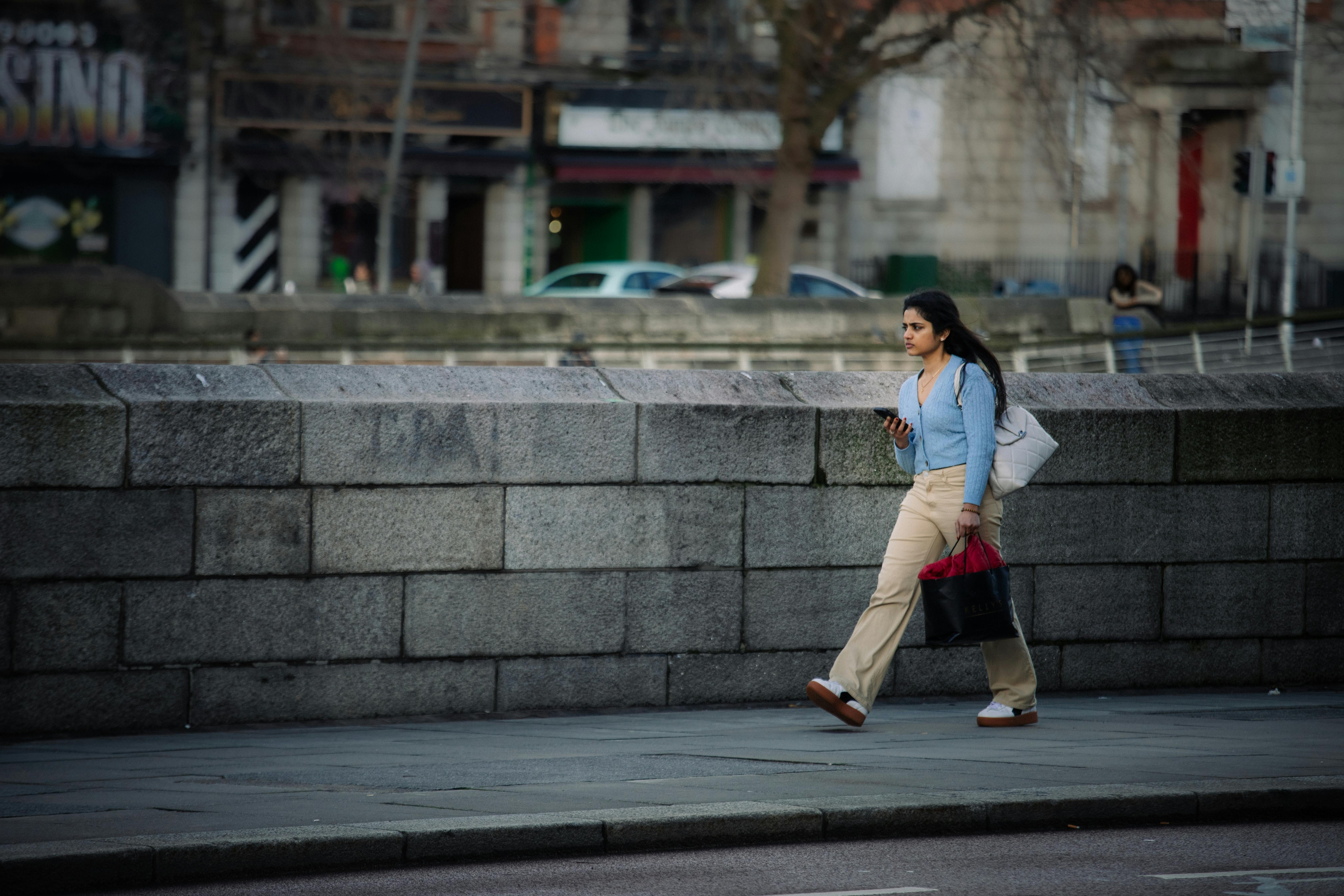 免费 一位身着休闲装的女子沿着都柏林市的石墙行走。 素材图片