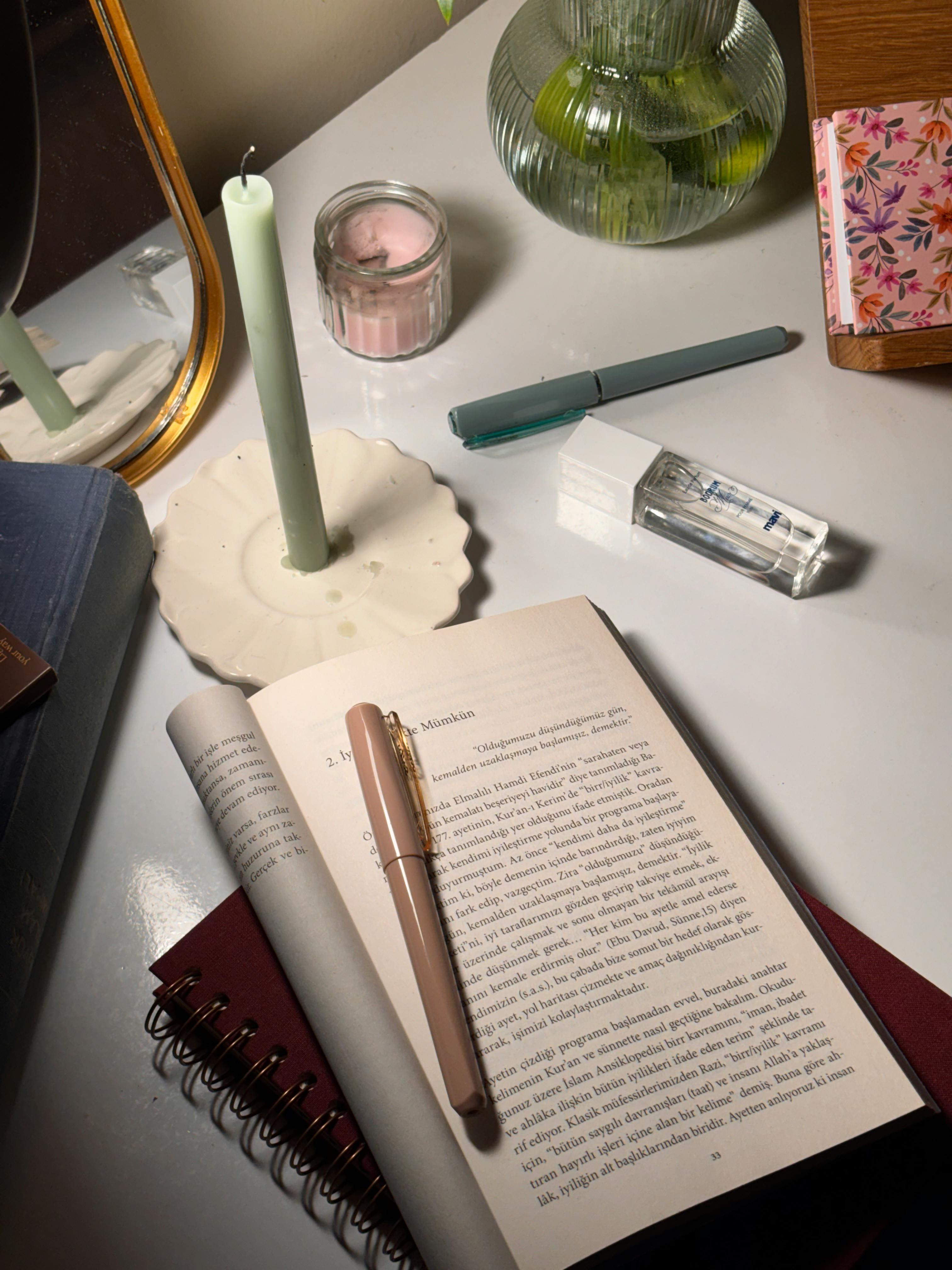 Gratis Calda scena da scrivania con un libro aperto, una candela e articoli di cancelleria per creare un'atmosfera rilassante. Foto a disposizione