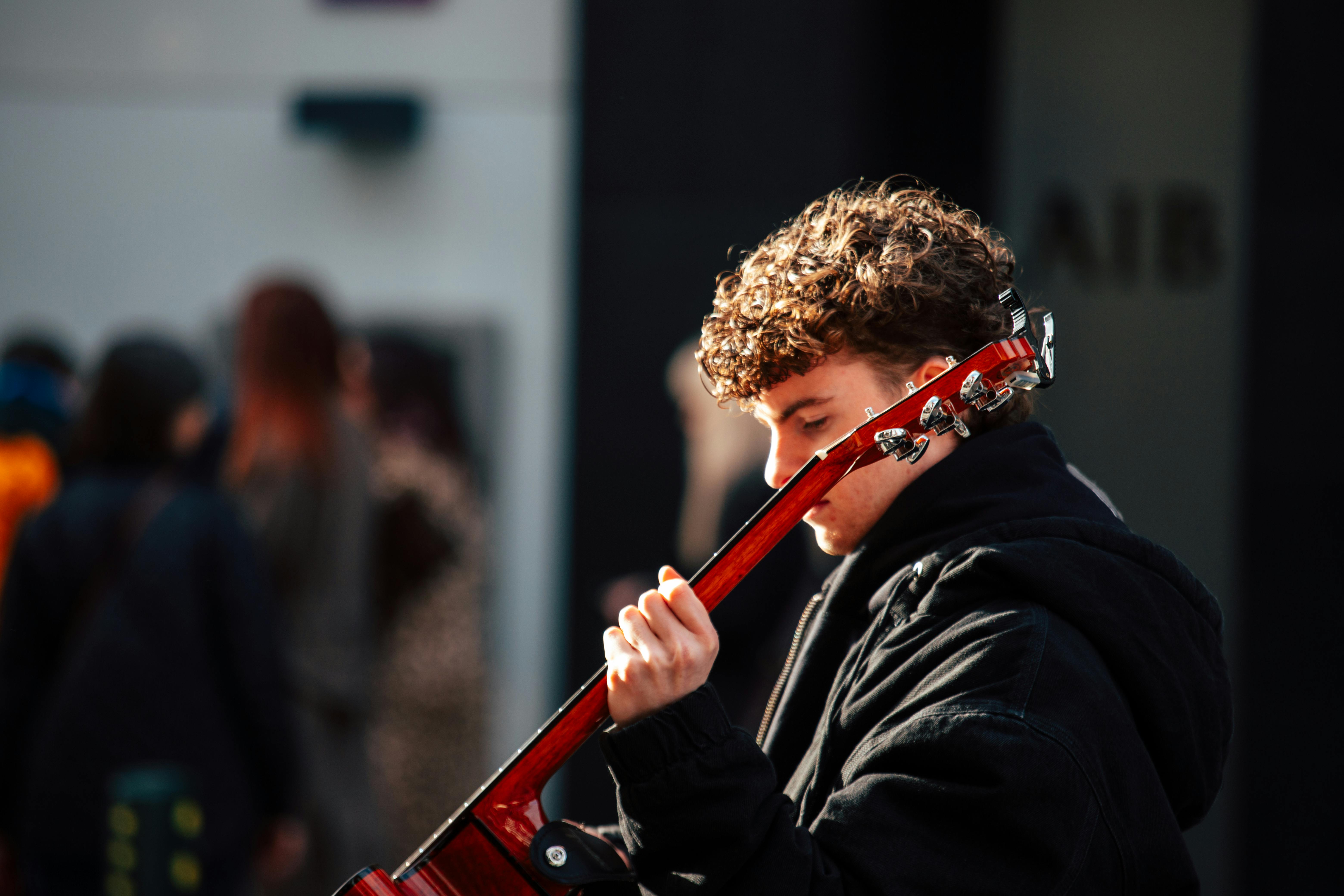 Bezpłatne Młody muzyk uliczny z kręconymi włosami gra na gitarze akustycznej w słoneczny dzień w Dublinie. Zdjęcie z galerii