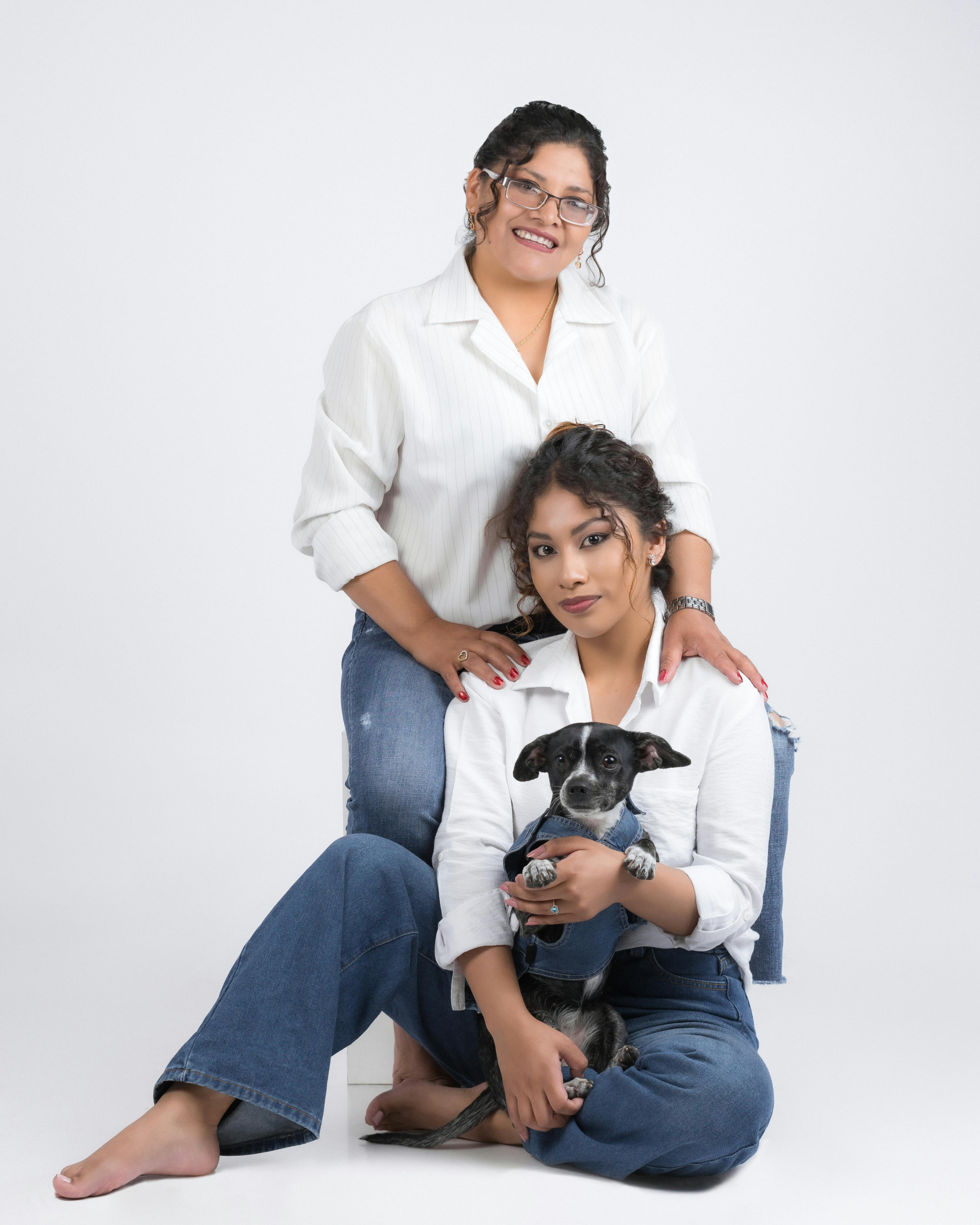 Gratis Donne sorridenti in abiti coordinati con un cagnolino in un ritratto in studio. Foto a disposizione