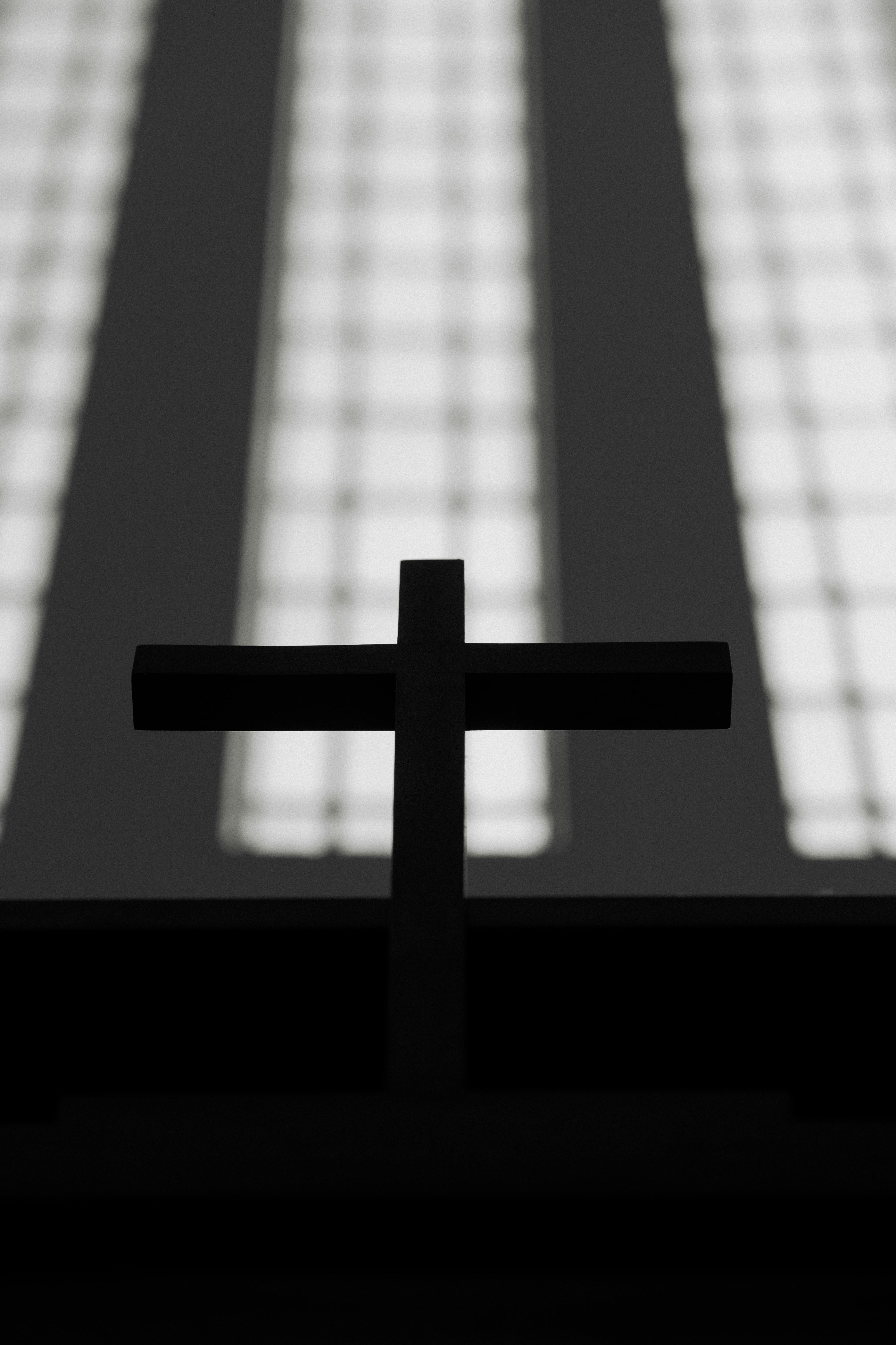 gratis Silhouet van een kerkkruis tegen een wazige raamachtergrond, wat een dramatisch effect creëert. Stockfoto