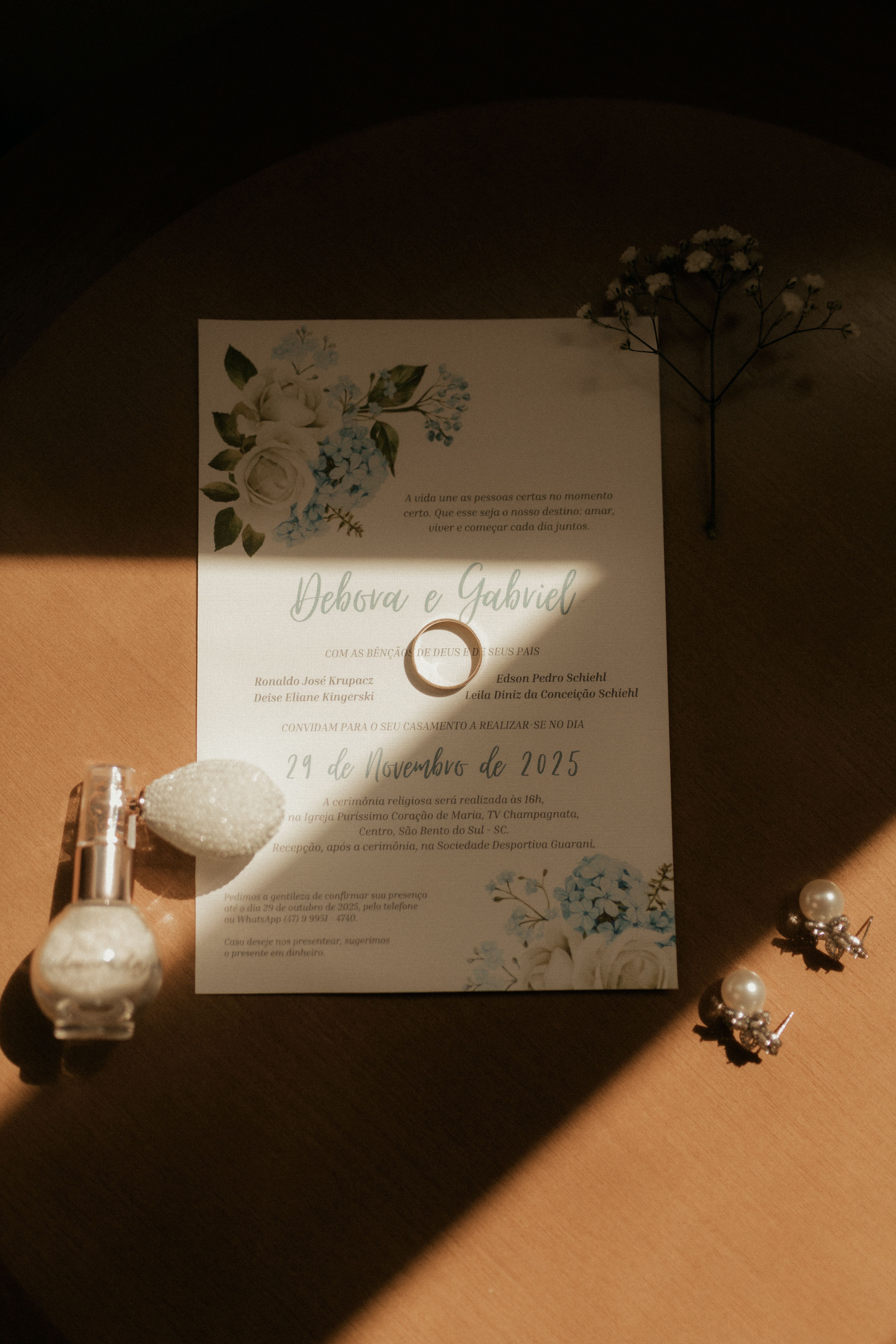 A beautifully designed wedding invitation with a ring and accessories on a wooden table in soft lighting.