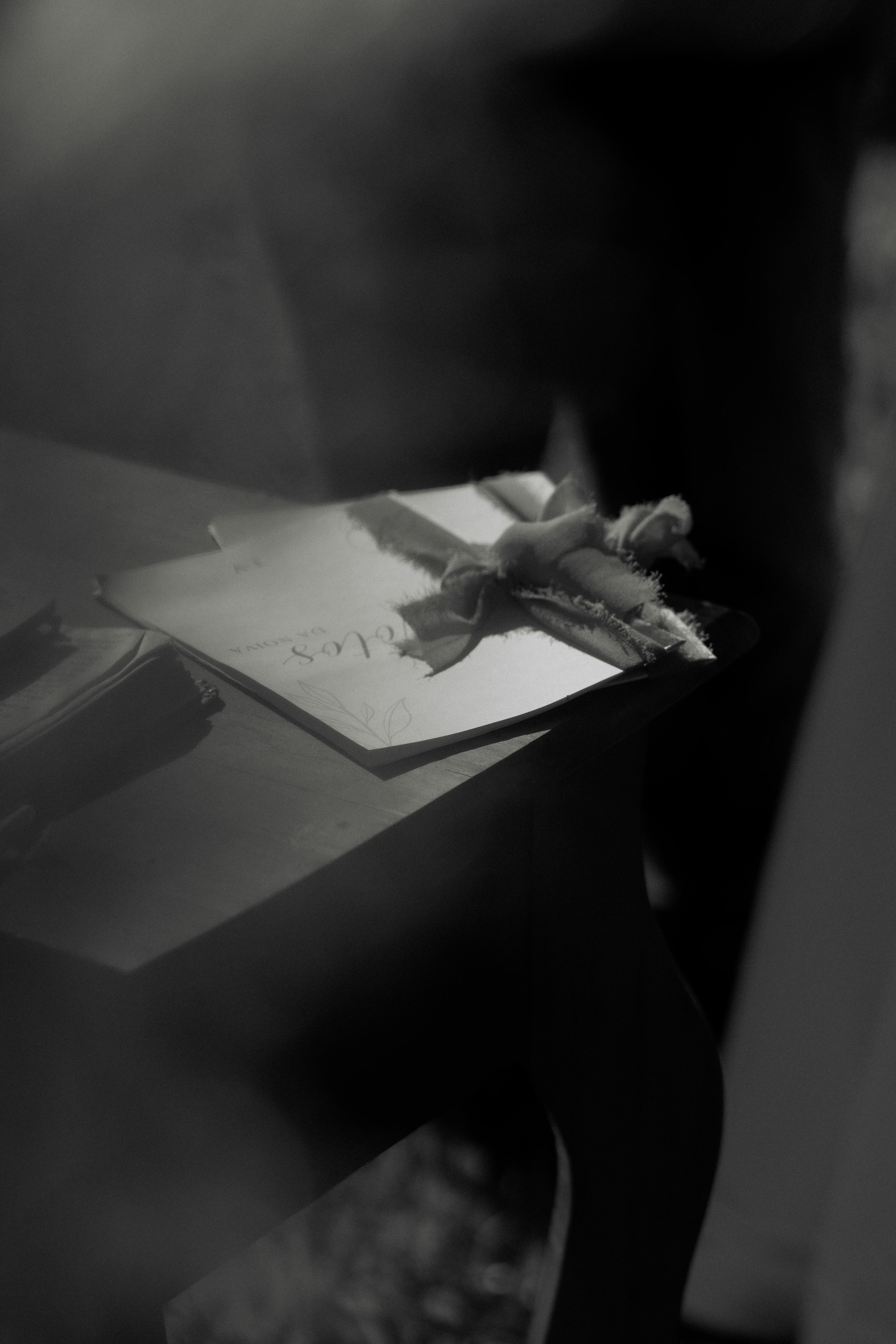 Kostenlos Elegantes Schwarz-Weiß-Foto einer Karte mit Schleife auf einem dunklen Schreibtisch. Stock-Foto