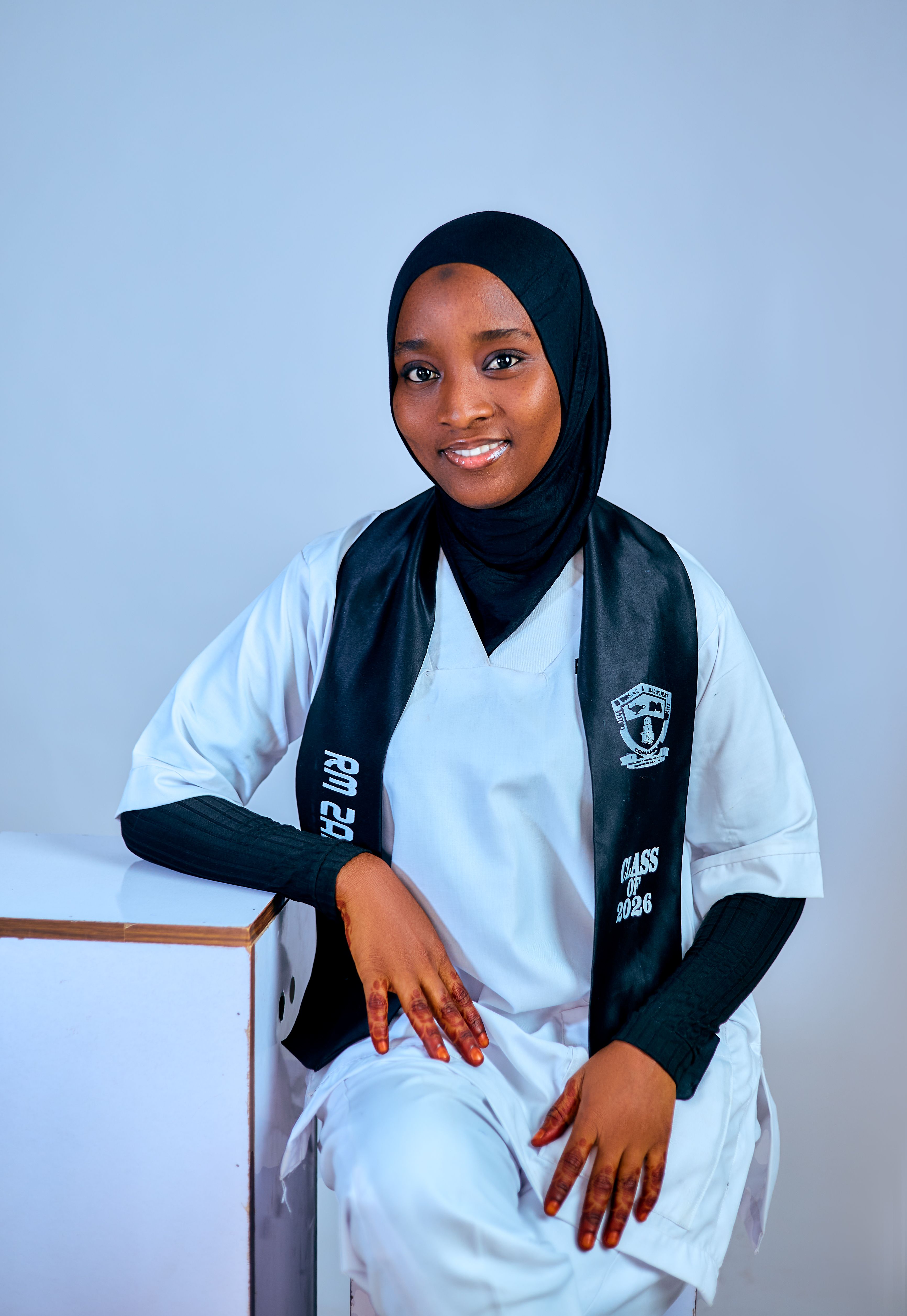Confident young graduate wearing a hijab and graduation gown against a neutral background.