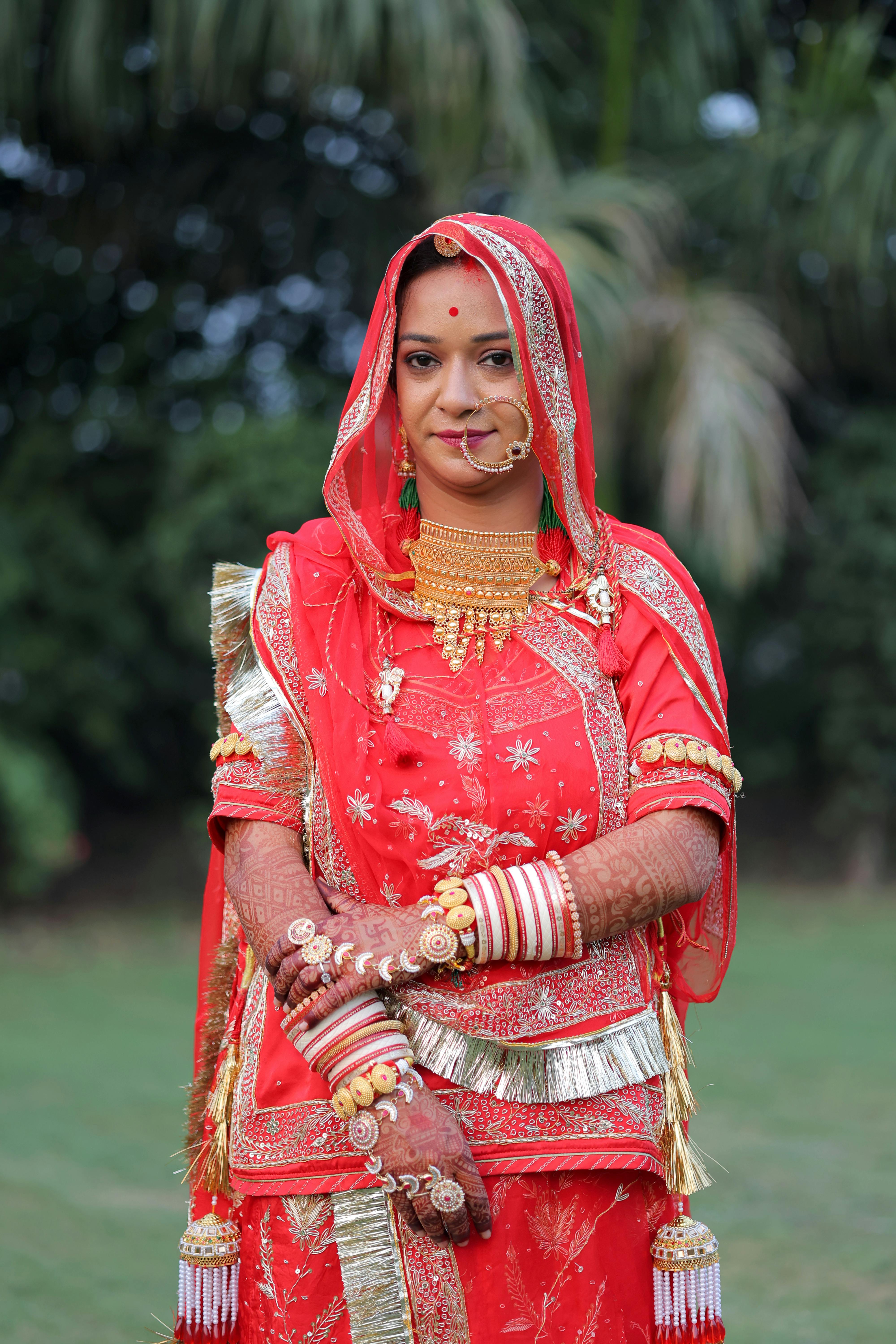 Δωρεάν Μια όμορφη Ινδή νύφη με παραδοσιακό κόκκινο σάρι, στολισμένη με κοσμήματα, ποζάρει σε εξωτερικό χώρο. Φωτογραφία από στοκ φωτογραφιών