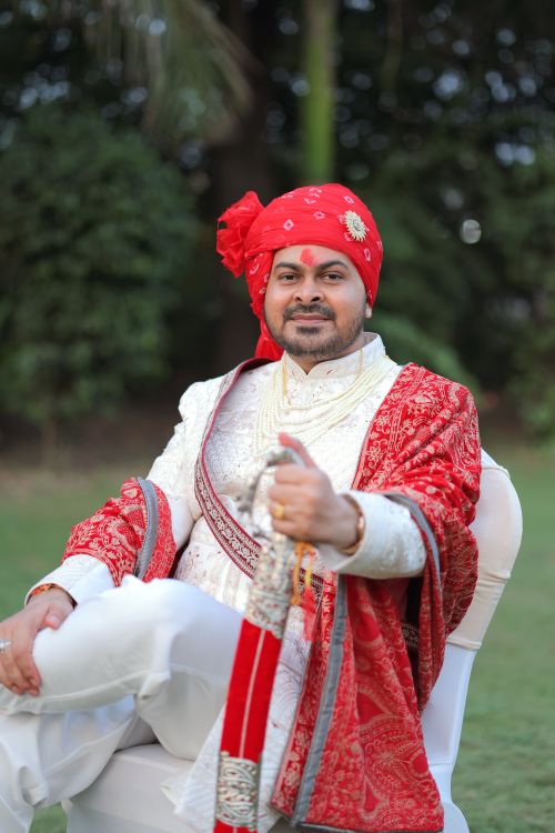 Free A confident Indian groom poses outdoors in traditional red and white wedding attire. Stock Photo