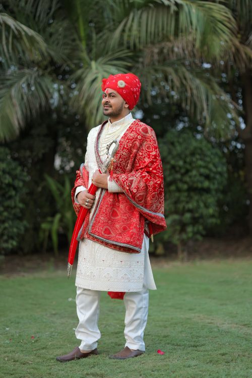 Free Indian groom in traditional red and white attire posing outdoors on a wedding day. Stock Photo