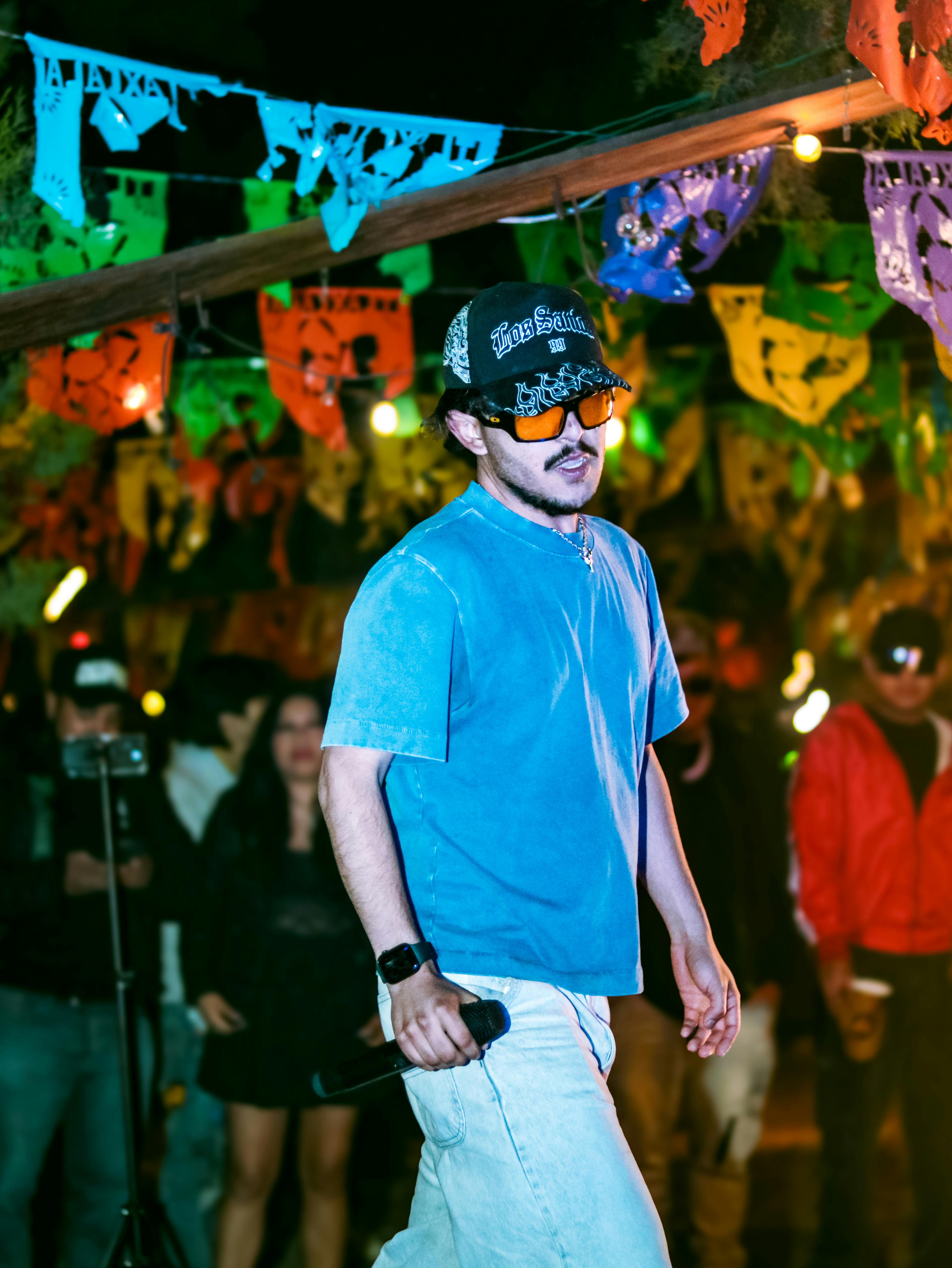 Δωρεάν Ένας νεαρός άνδρας ερμηνευτής τραγουδάει σε ένα υπαίθριο νυχτερινό φεστιβάλ με πολύχρωμες διακοσμήσεις. Φωτογραφία από στοκ φωτογραφιών