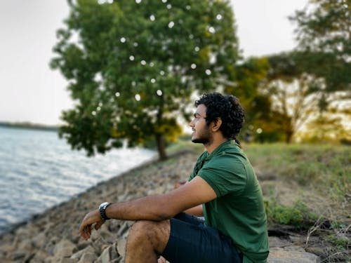 無料 水域の近くの岩の上に座っている緑のtシャツと青のデニムジーンズの男 写真素材