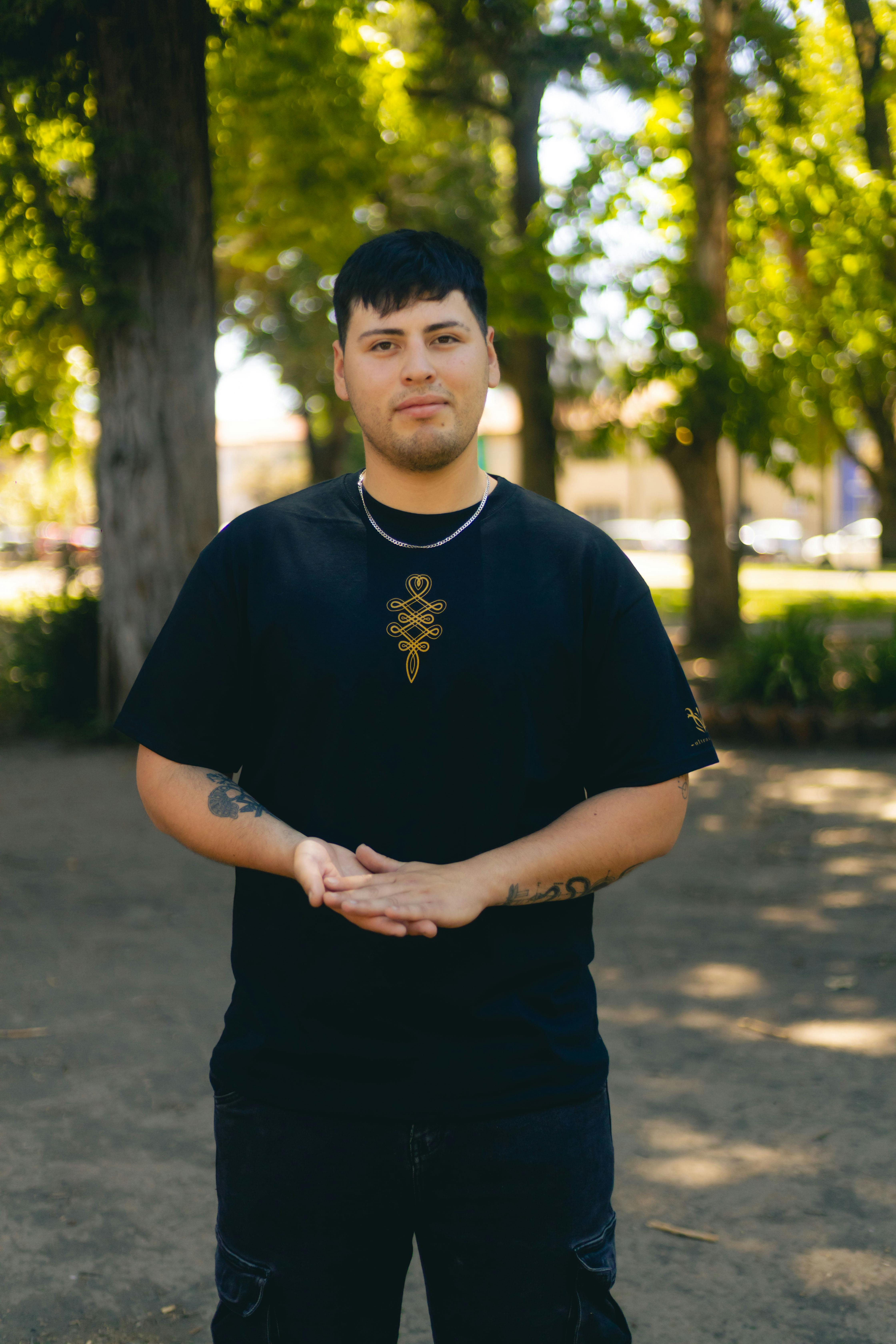 Miễn phí Chàng trai trẻ đứng thư thái trong một công viên ngập nắng với cây cối phía sau. Ảnh lưu trữ