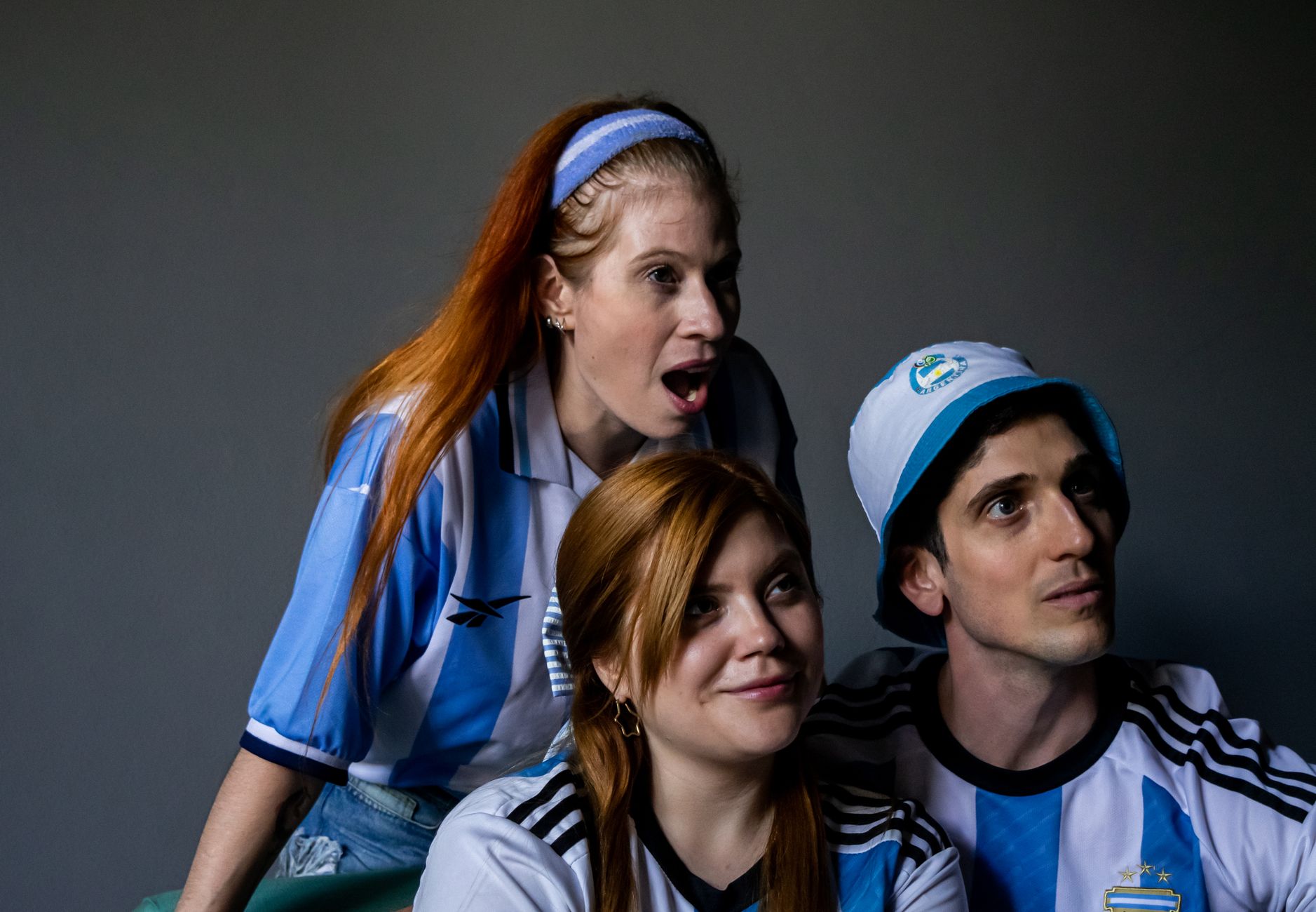 Group of enthusiastic fans in Argentina jerseys cheering passionately indoors.