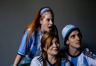 Group of enthusiastic fans in Argentina jerseys cheering passionately indoors.