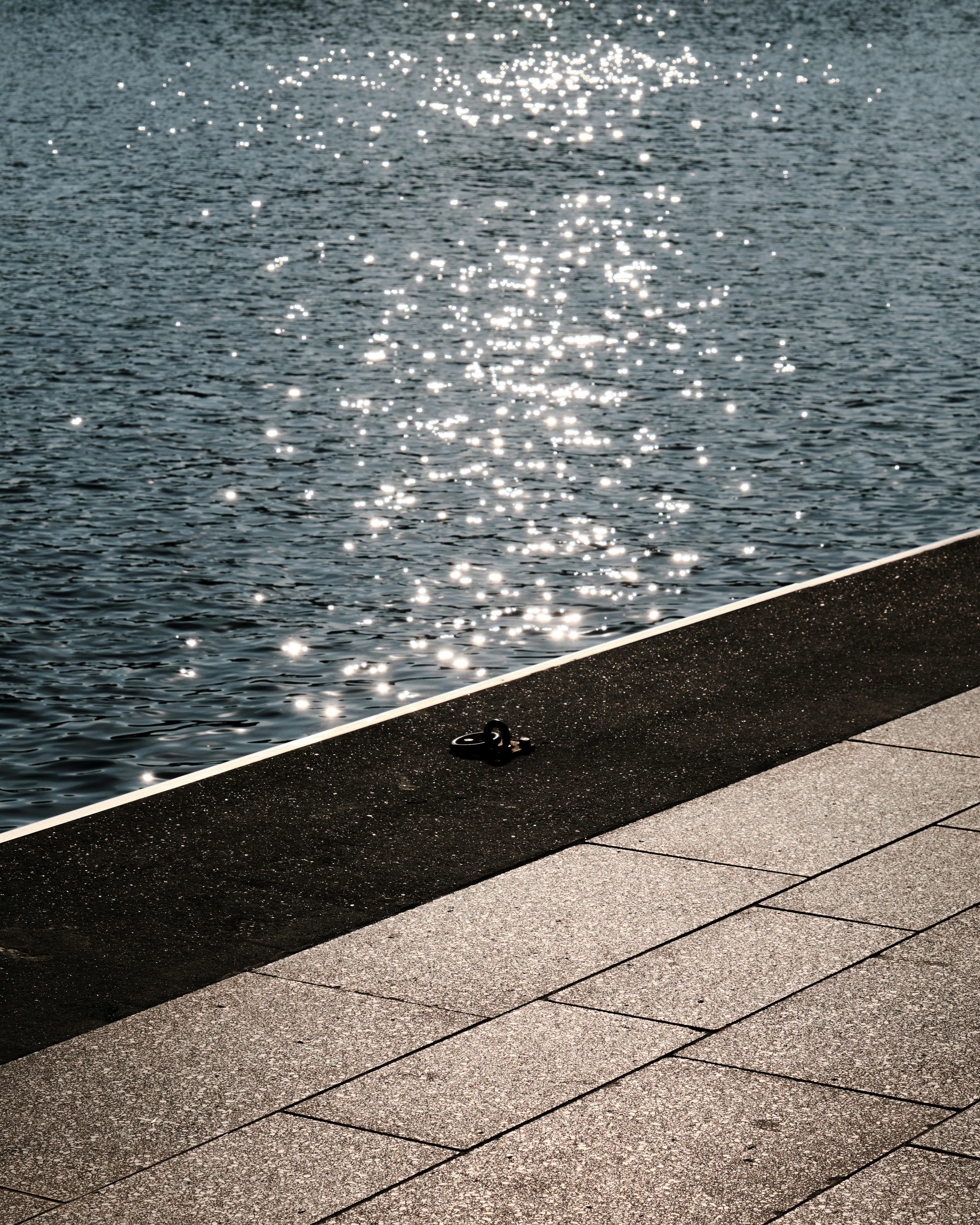 Zadarmo Odlesky slnečného svetla sa trblietajú na vode vedľa dláždeného chodníka v Hamburgu v Nemecku. Fotka z fotobanky