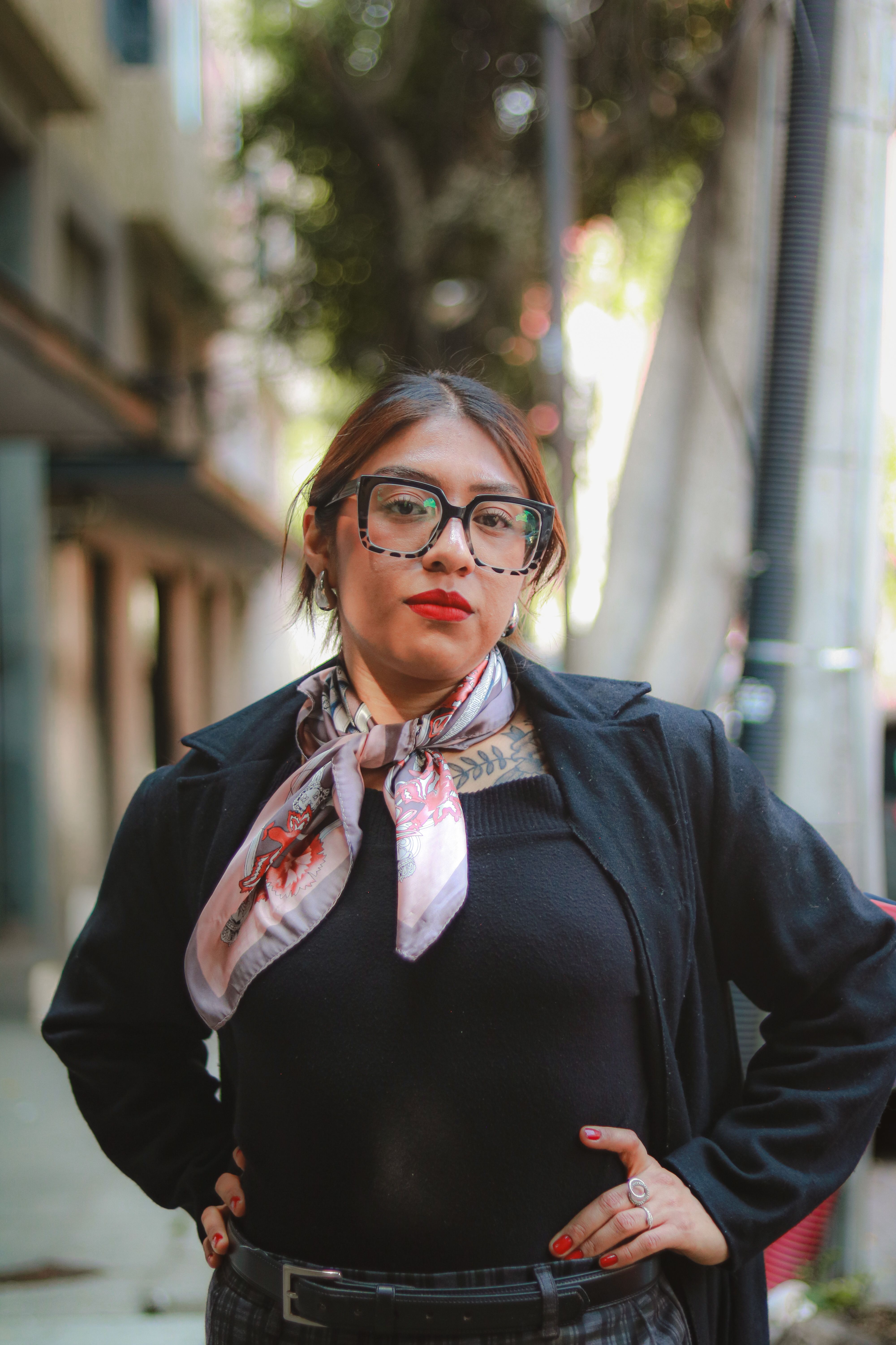 Confident woman posing outdoors. Fashionable look with scarf and glasses. Strong and assertive stance.