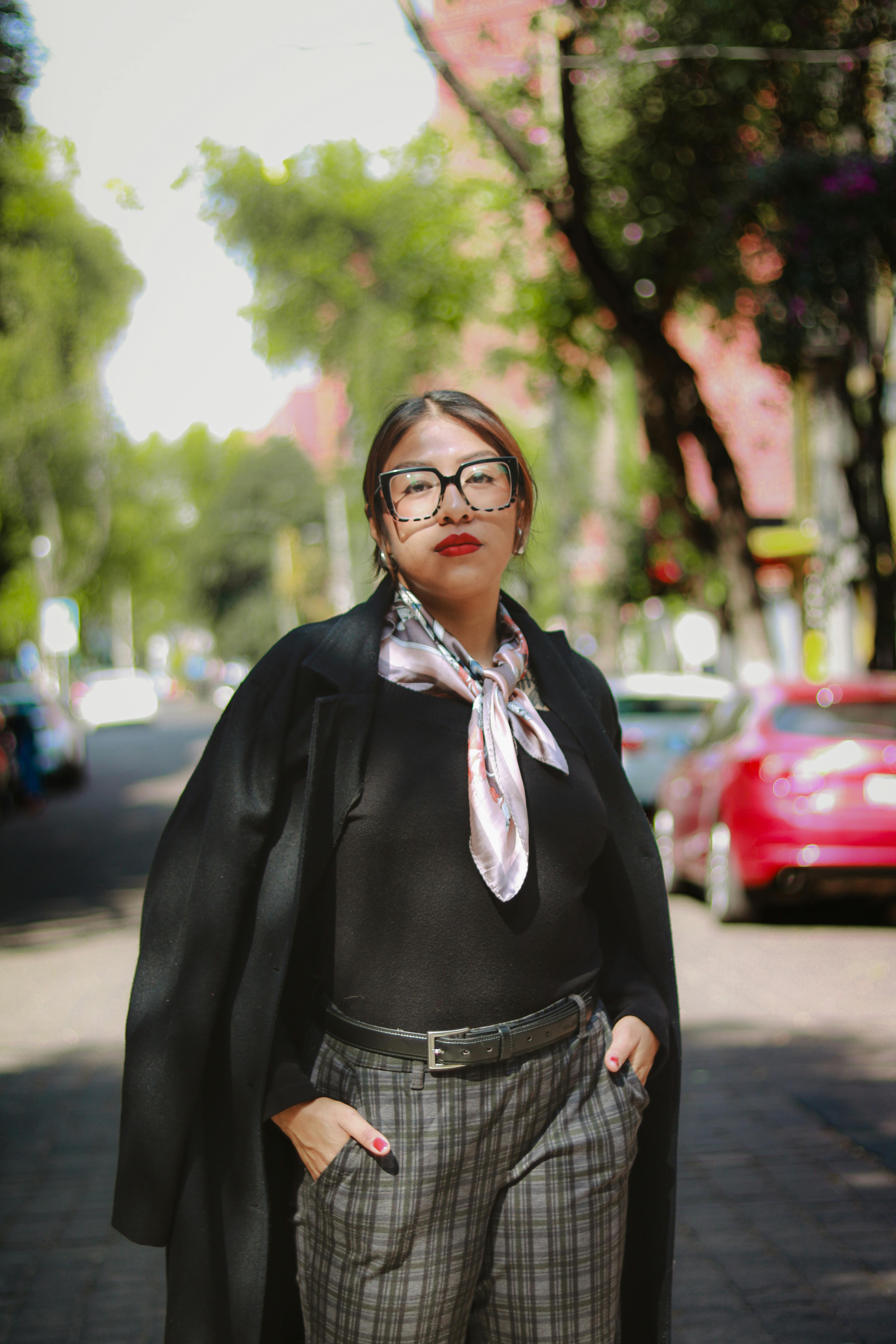 Gratis Una donna vestita con stile posa con sicurezza in una strada urbana illuminata dal sole. Foto a disposizione