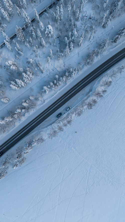 Free Stunning aerial photo capturing a winter road dividing a snowy forest and open field. Stock Photo
