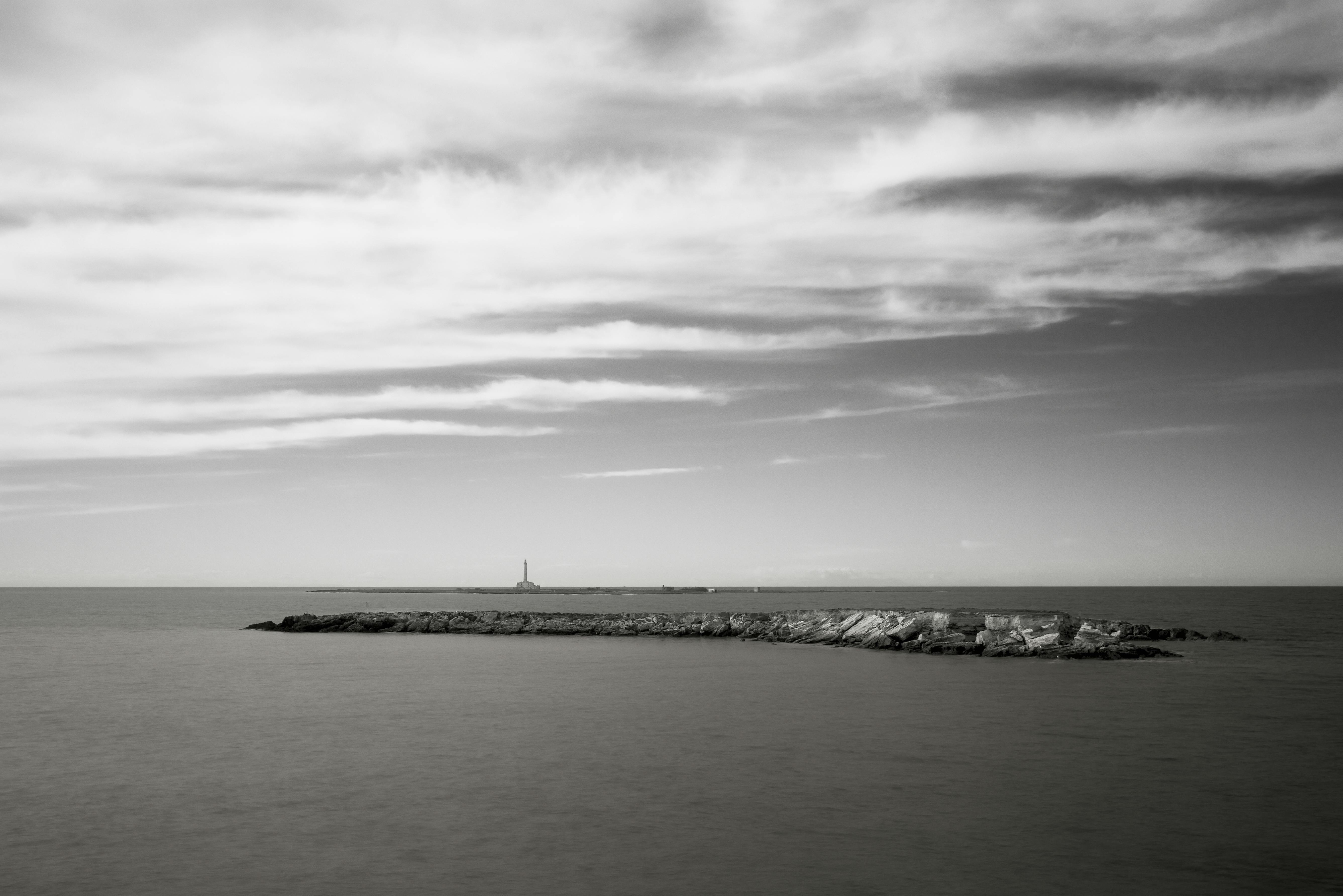 Kostenlos Ruhige Küstenansicht in Schwarz-Weiß mit Leuchtturm und Felsvorsprung. Stock-Foto