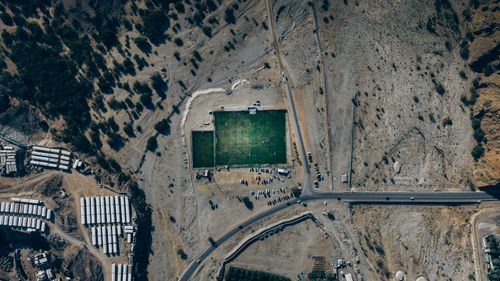 Free Drone shot of a soccer field amidst the desert terrain in Oman, showcasing rugged landscapes and rural sports facilities. Stock Photo