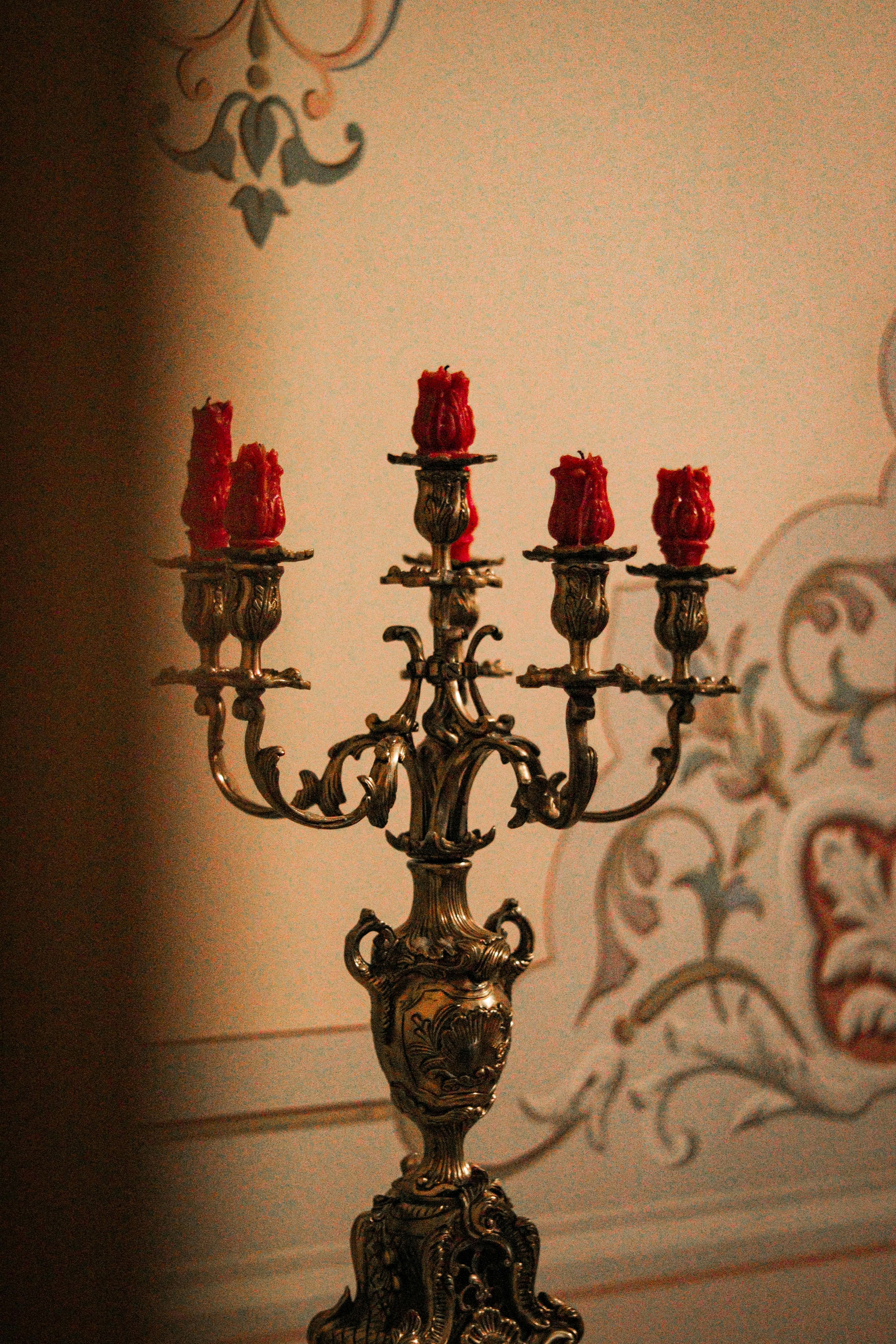 Gratis Un candelabro decorativo vintage con candele rosse, posizionato su una parete decorata con motivi ornamentali. Foto a disposizione