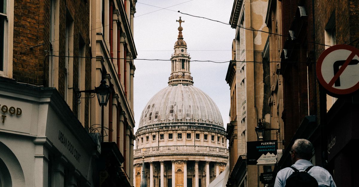 A dramatic view of St Paul s Cathedral framed by narrow London streets at daytime.