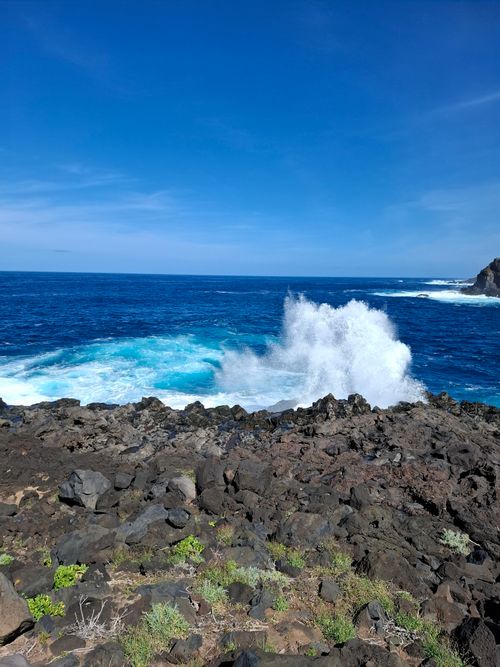 Free Powerful ocean wave crashes on rocky shore under clear blue sky, capturing nature's raw power. Stock Photo