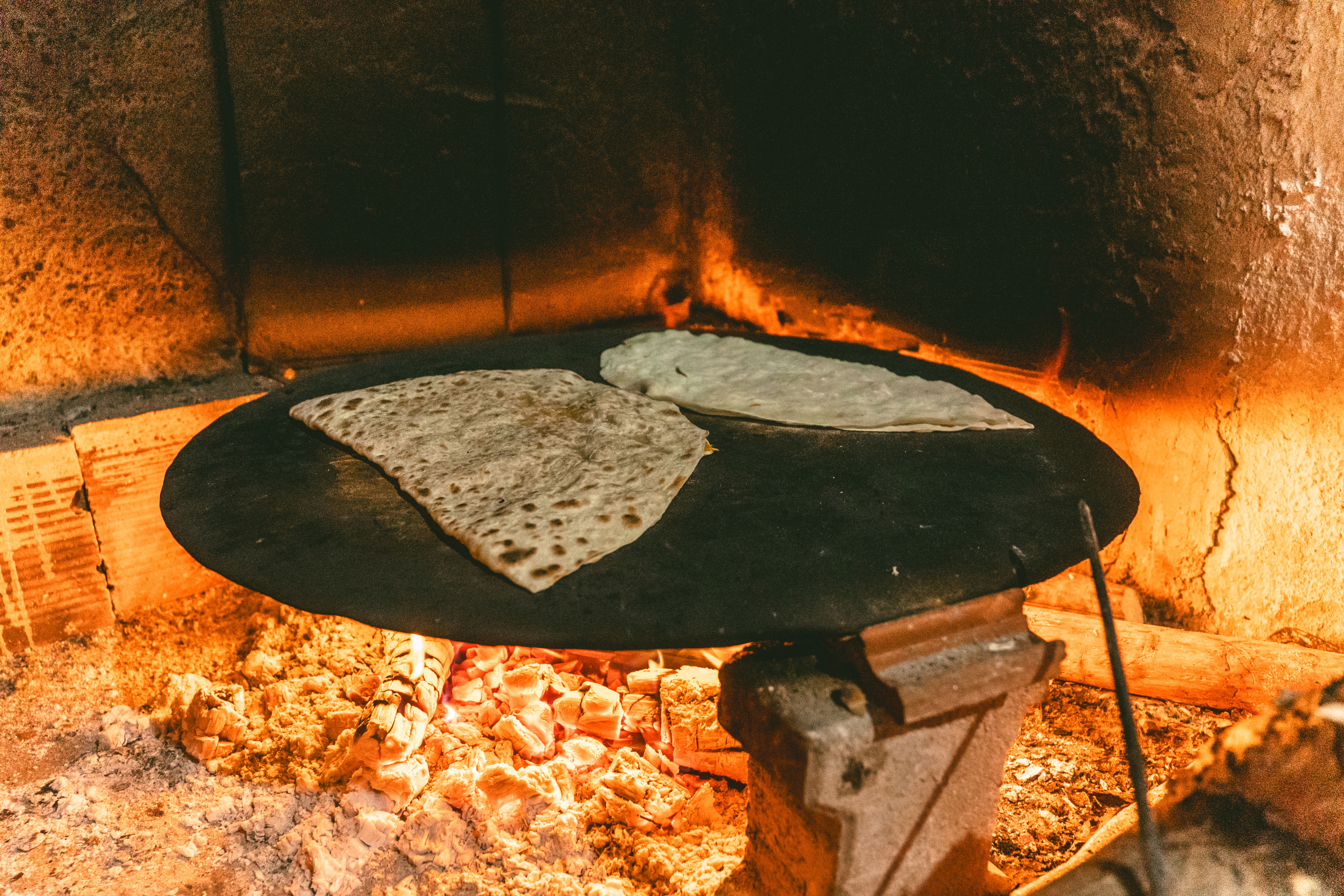 Delicious Turkish flatbread being baked on a metal surface over an open flame inside a stone oven.