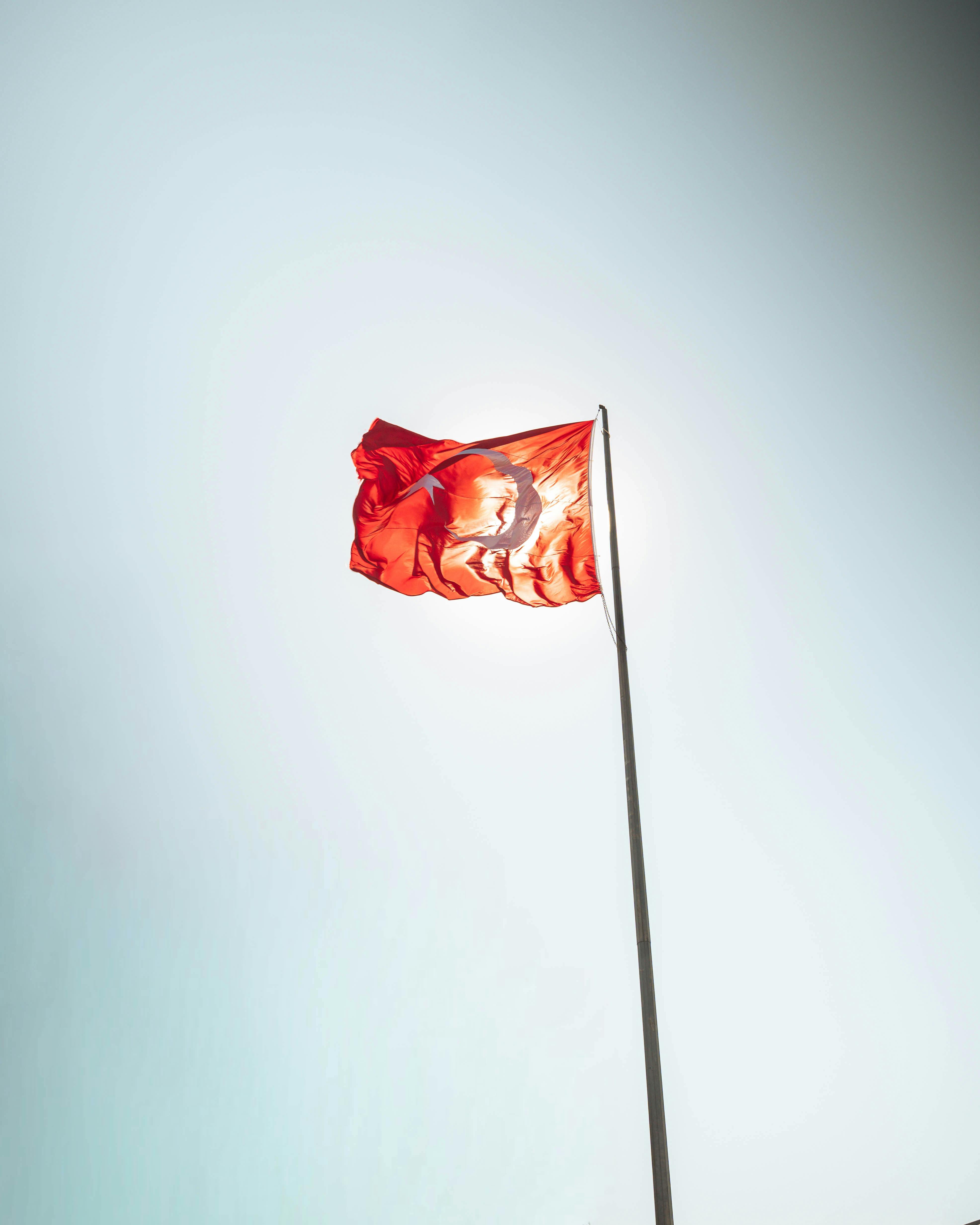 Free Red Turkish flag with crescent and star fluttering against a bright, clear sky, symbolizing national pride. Stock Photo
