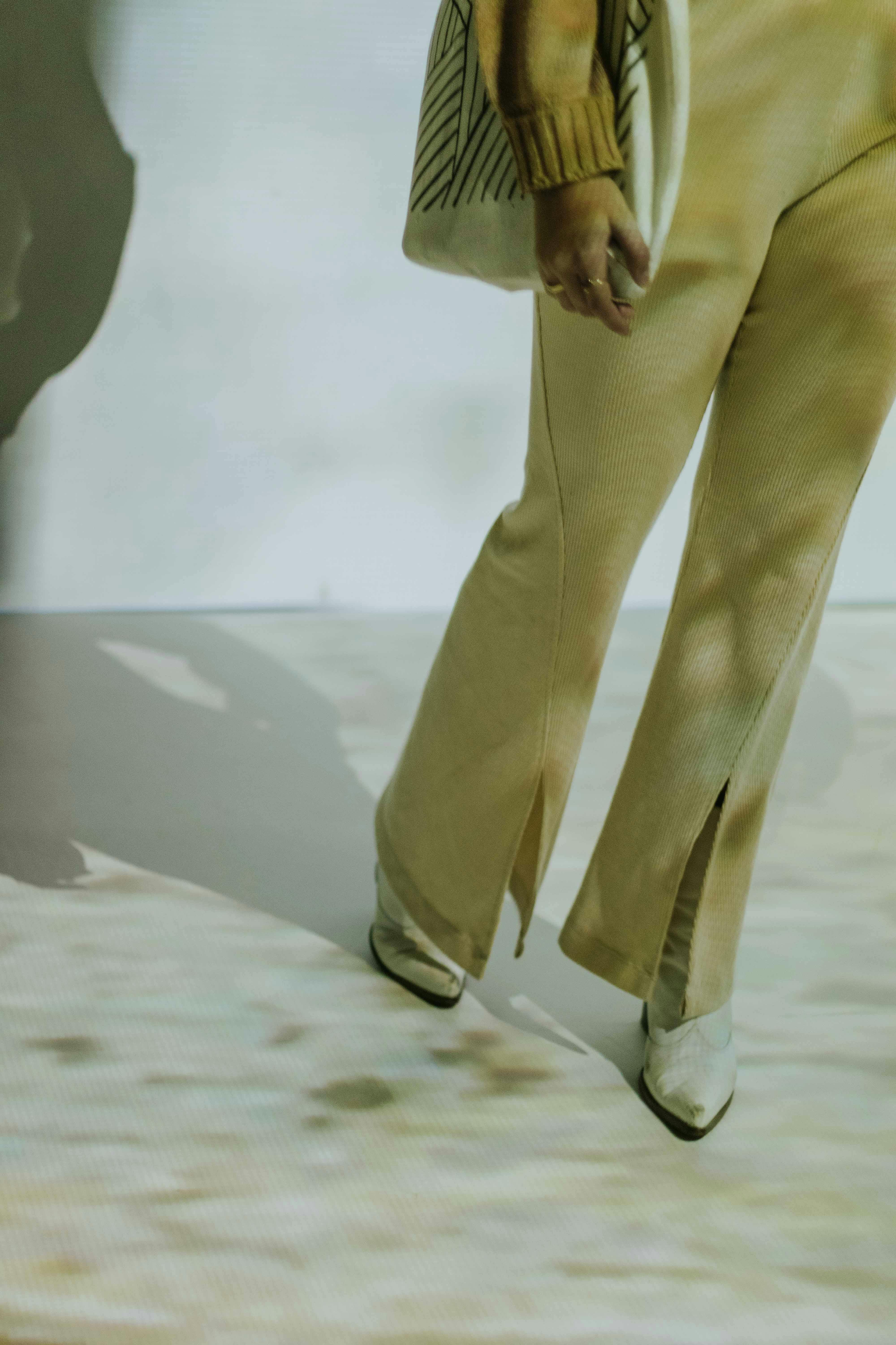 Gratis Donna elegante con pantaloni beige e stivali, che mette in risalto effetti creativi di luci e ombre. Foto a disposizione