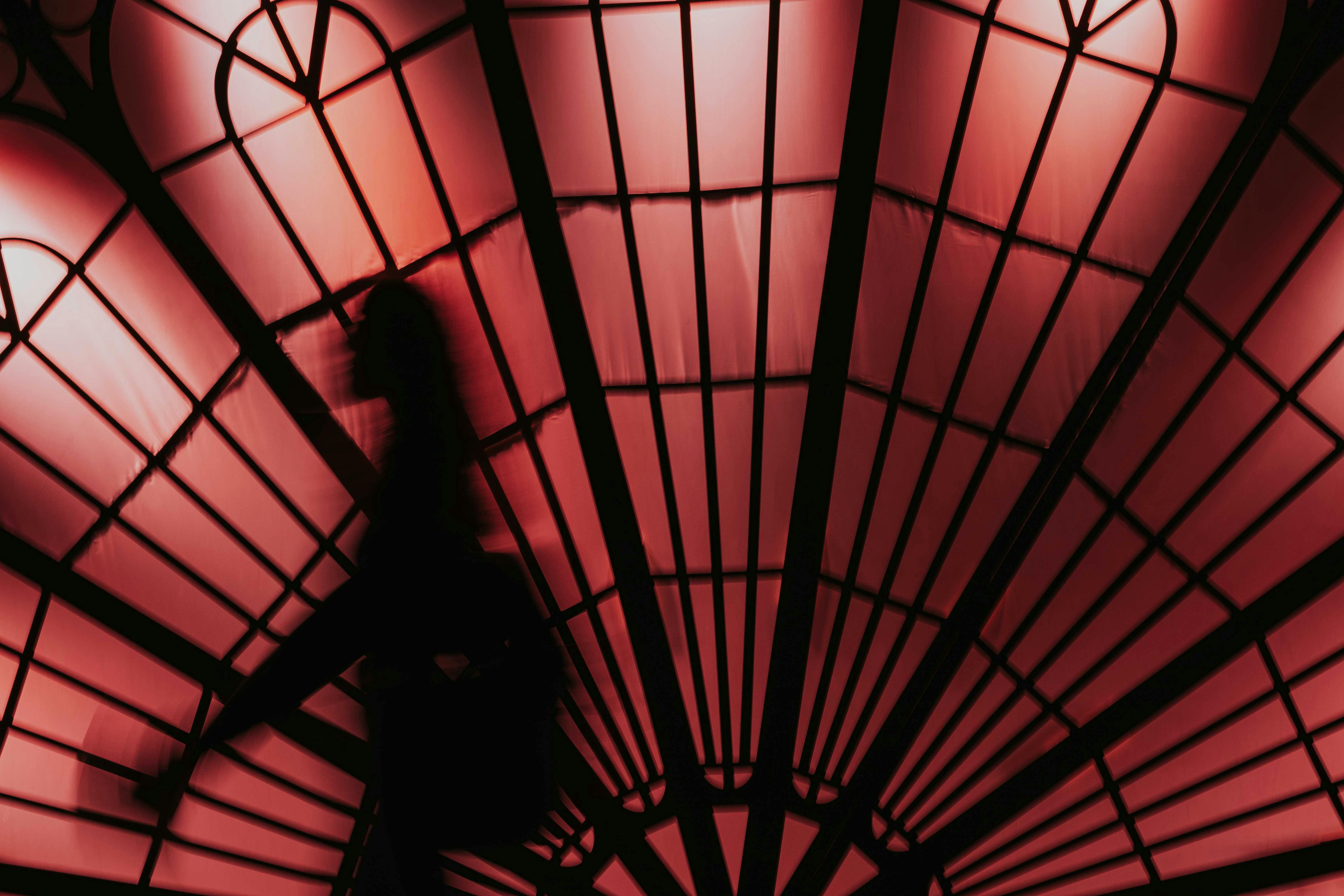 Gratuit Silhouette d'une personne marchant devant un grand vitrail rouge en forme d'éventail. Photos