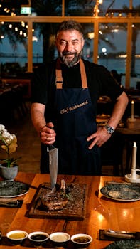 Chef in apron presenting a grilled dish in a cozy seaside restaurant, evening ambiance.