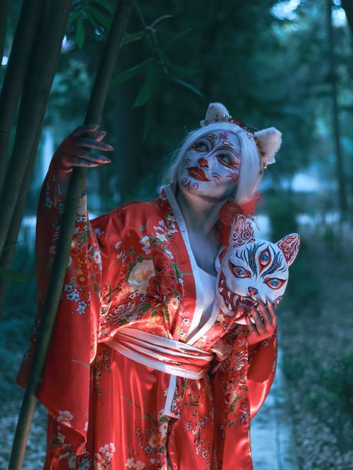 Free A captivating image of a woman in a fox-themed kimono holding a mask in a forest setting. Stock Photo