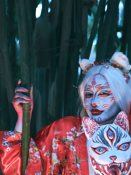 Free A mythical figure in a red kimono and face paint, posing in a bamboo forest. Stock Photo