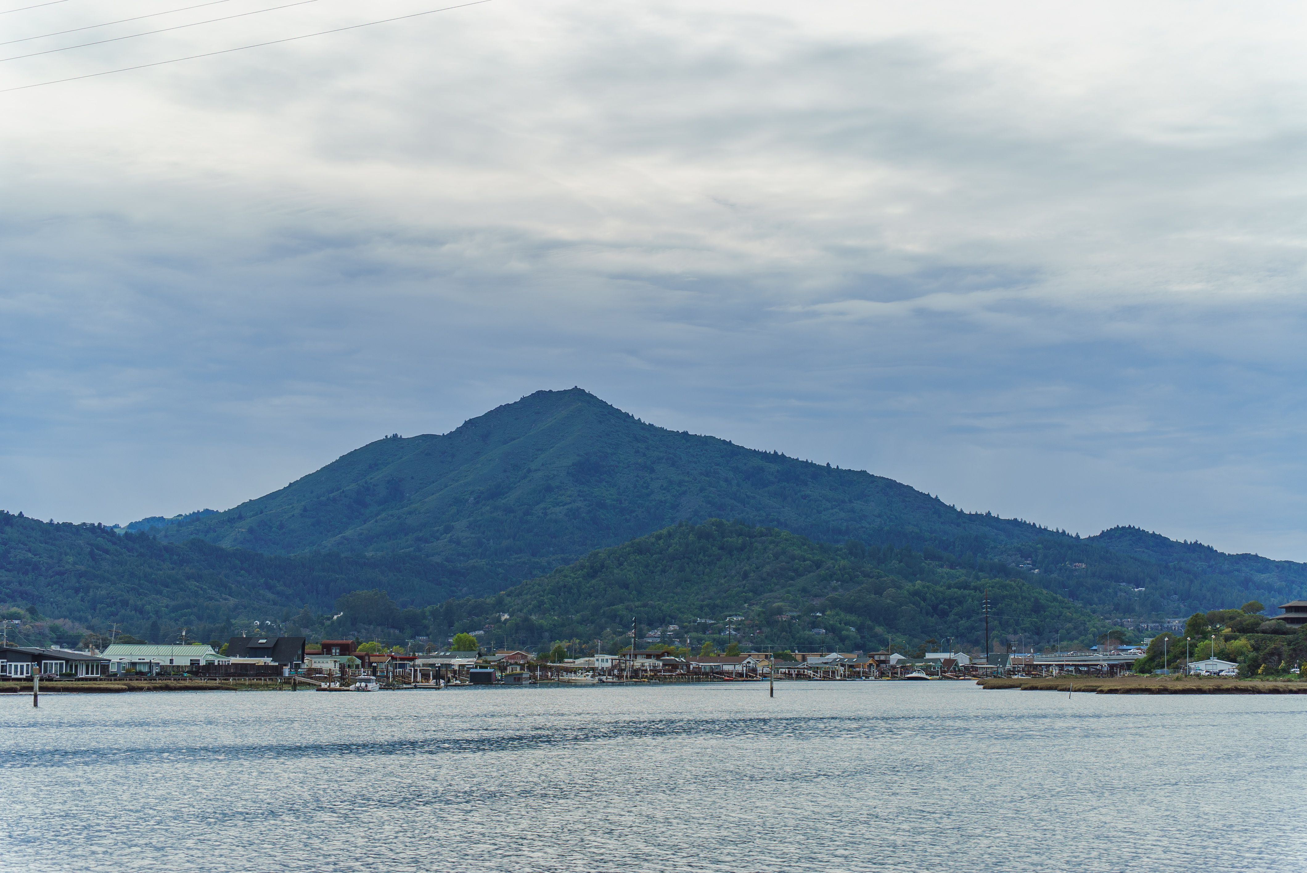 A picturesque view of a mountain and village across the water on a cloudy day.