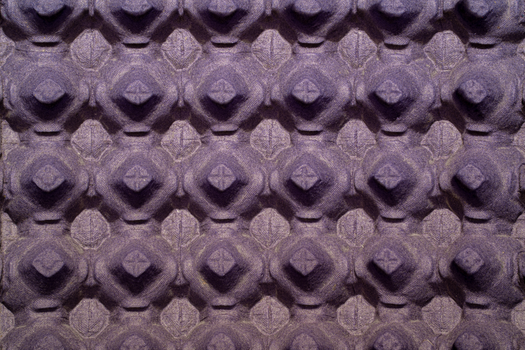 Close-up view of a textured purple egg carton surface with a repeating pattern.