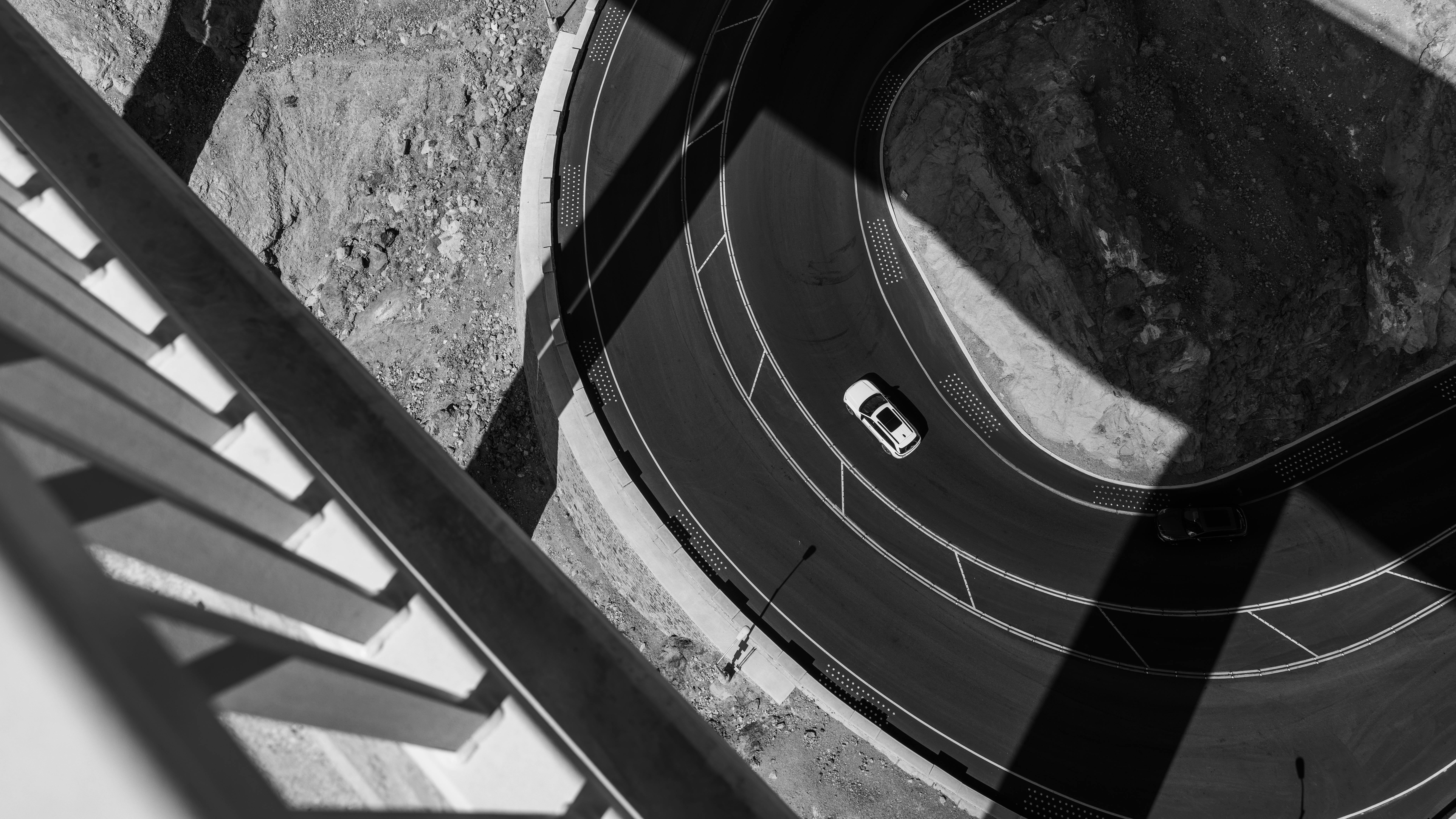 Gratis Un automóvil circula por una carretera sinuosa, proyectando sombras dramáticas en una escena en blanco y negro. Foto de stock