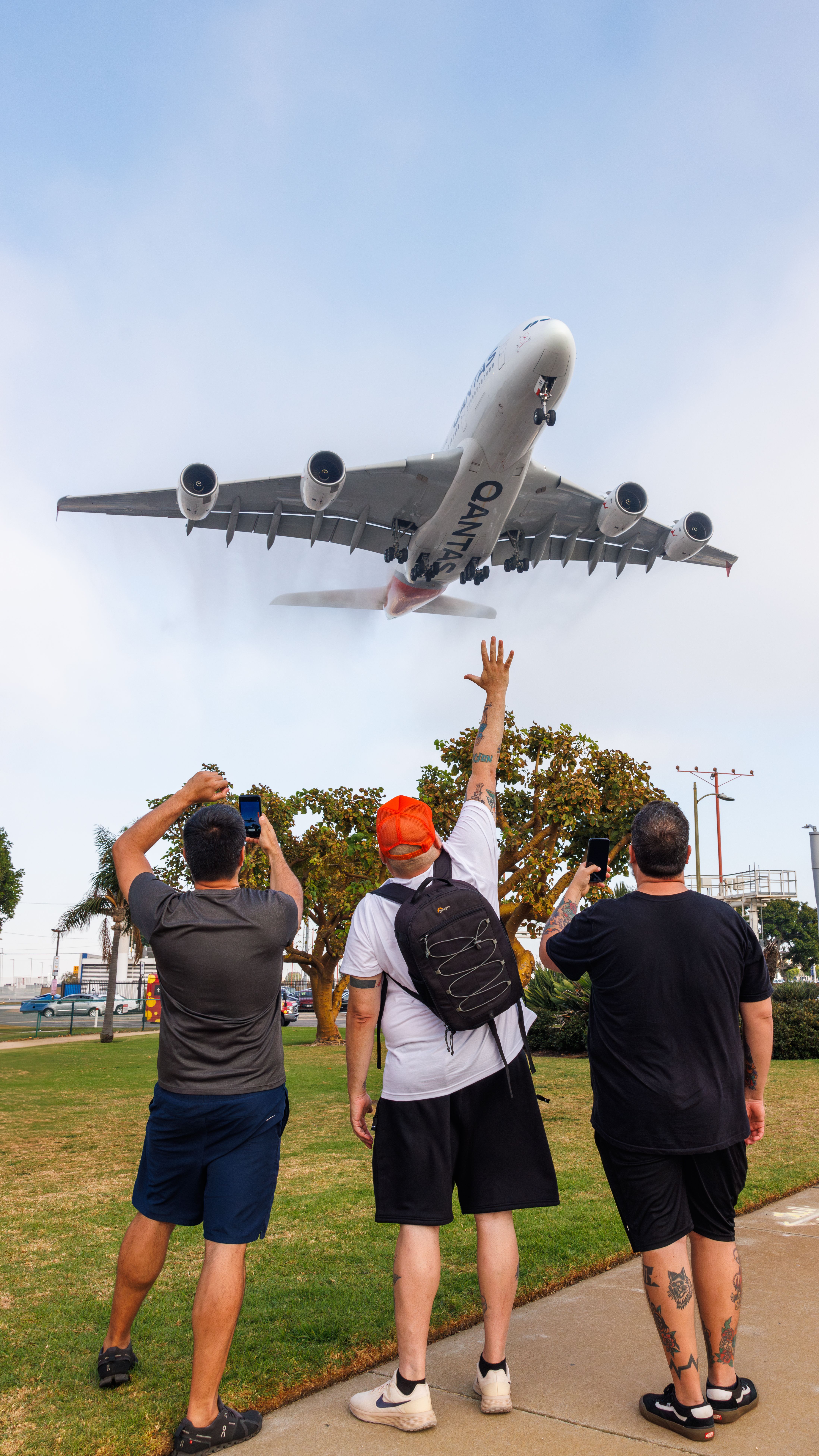 Three people watch a low-flying Qantas airplane at Los Angeles' famous spotting location.
