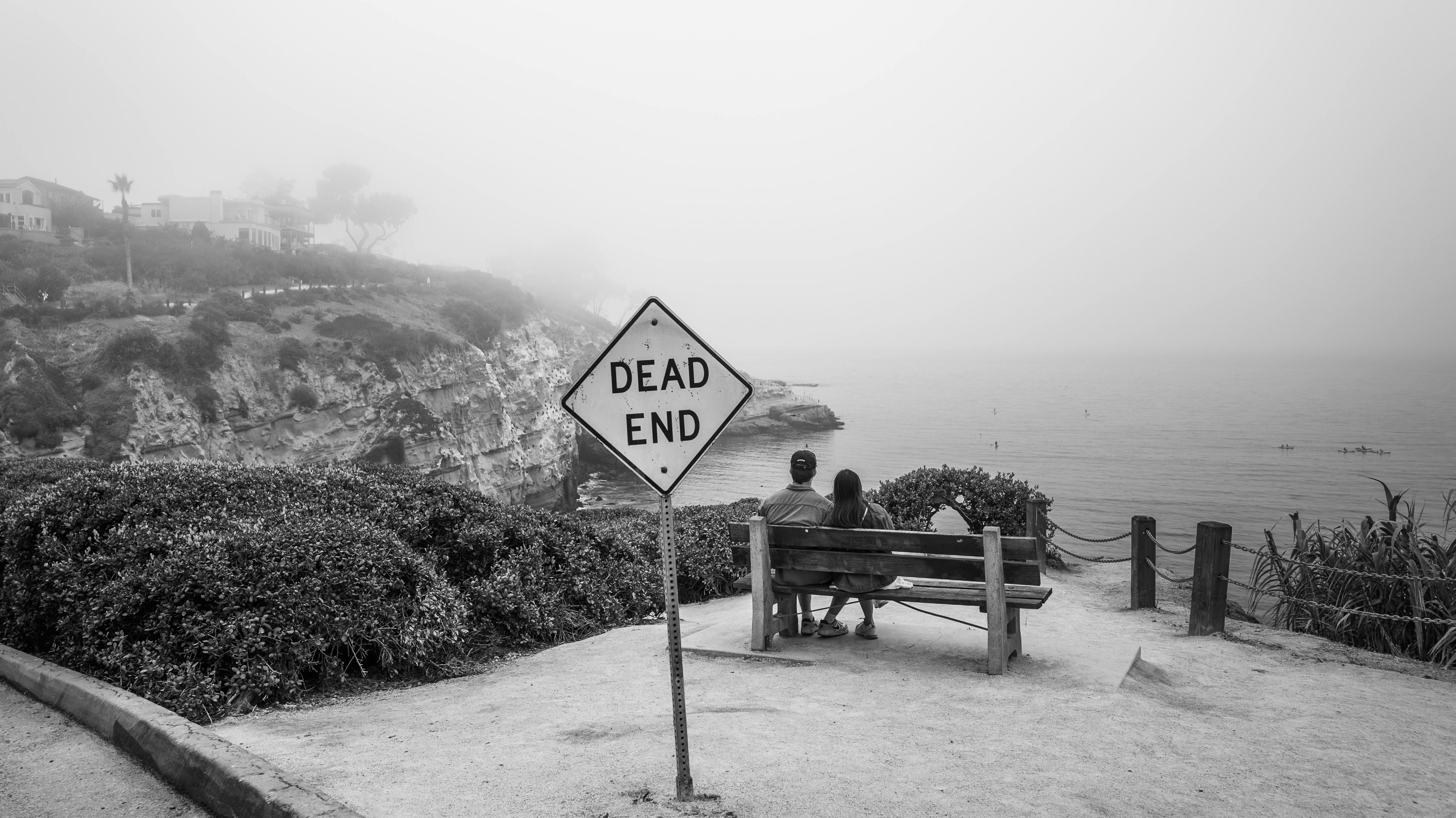 Miễn phí Một cặp đôi ngồi trên băng ghế bên vách đá có biển báo "Đường cụt", bao phủ bởi sương mù. Ảnh lưu trữ