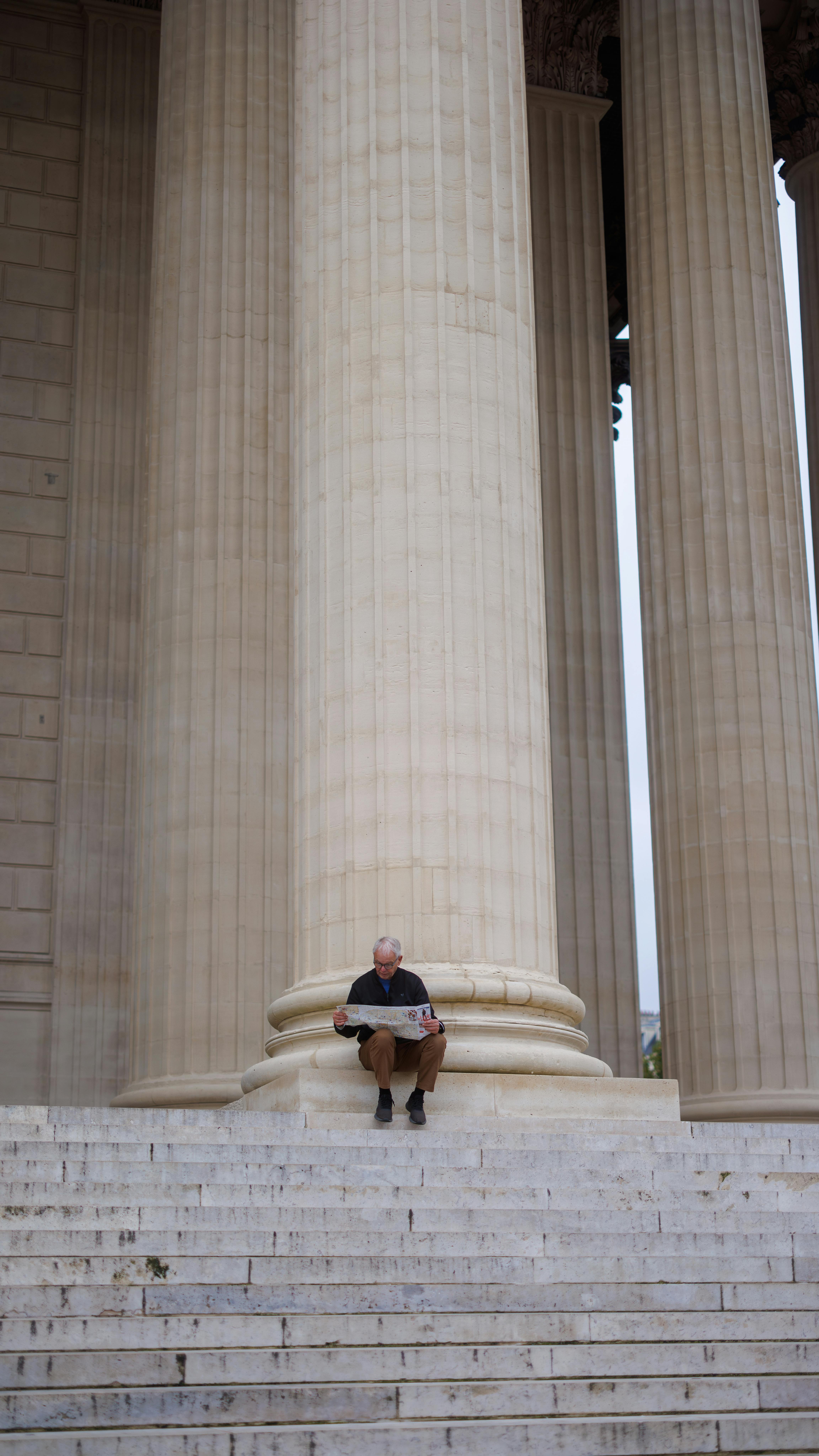 A man sits reading on the steps of a large historic monument with towering columns.