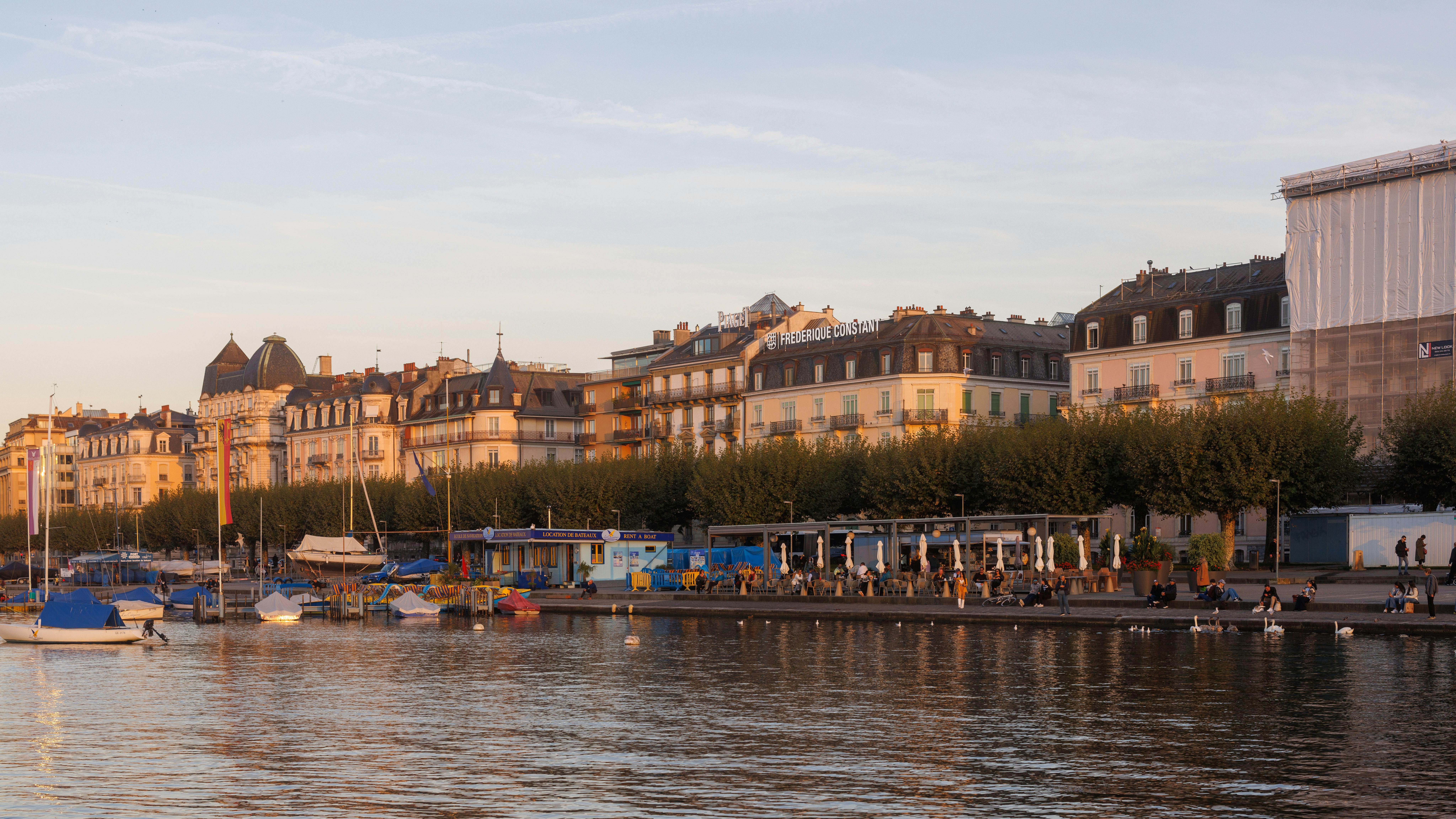 Beautiful sunset view of a waterfront in Geneva, Switzerland, with historic buildings and boats.