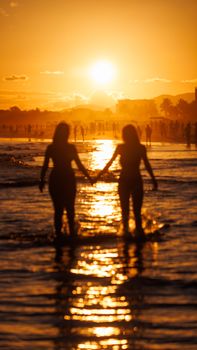 Silhouetted figures holding hands on a beach during a vivid sunset, reflecting warmth and connection.