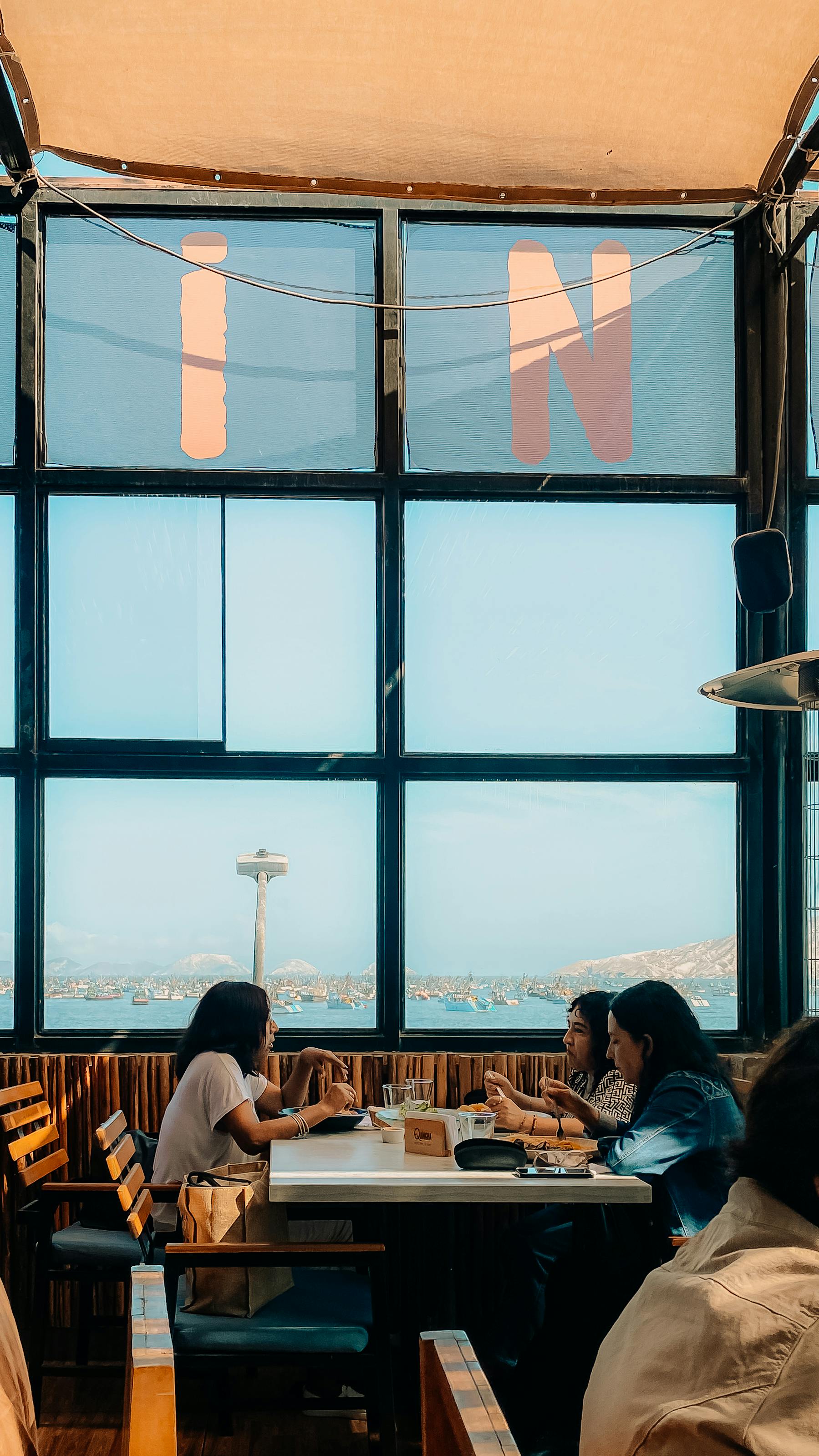 Δωρεάν Μια ομάδα ενηλίκων απολαμβάνει ένα γεύμα σε ένα καφέ με όμορφη θέα στον ωκεανό. Φωτογραφία από στοκ φωτογραφιών