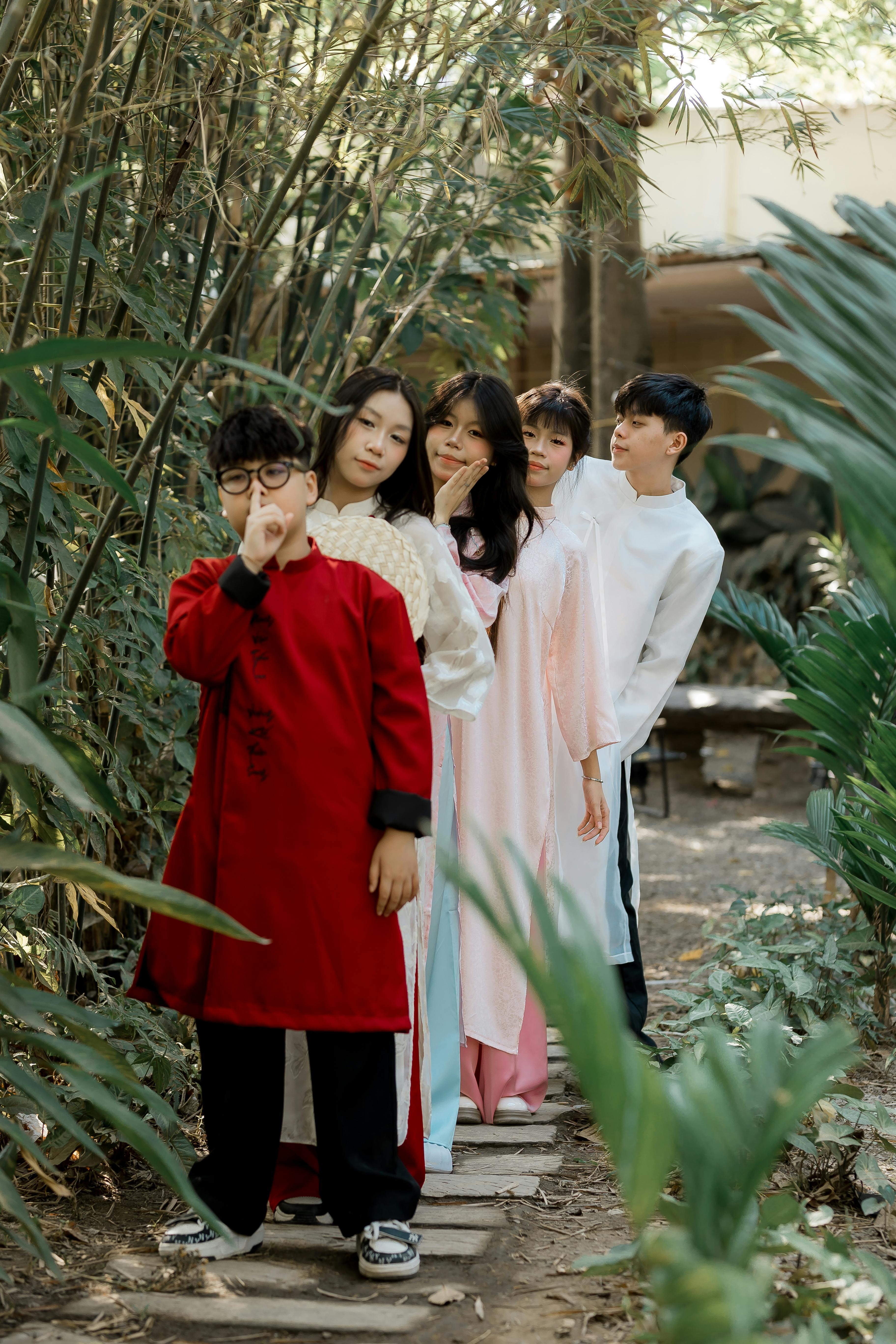 A group of people in traditional Asian attire stand on an outdoor path surrounded by foliage.