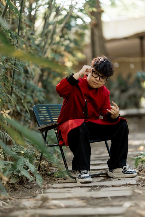 Free Teenager in red coat playing air guitar in a green garden setting during the day. Stock Photo