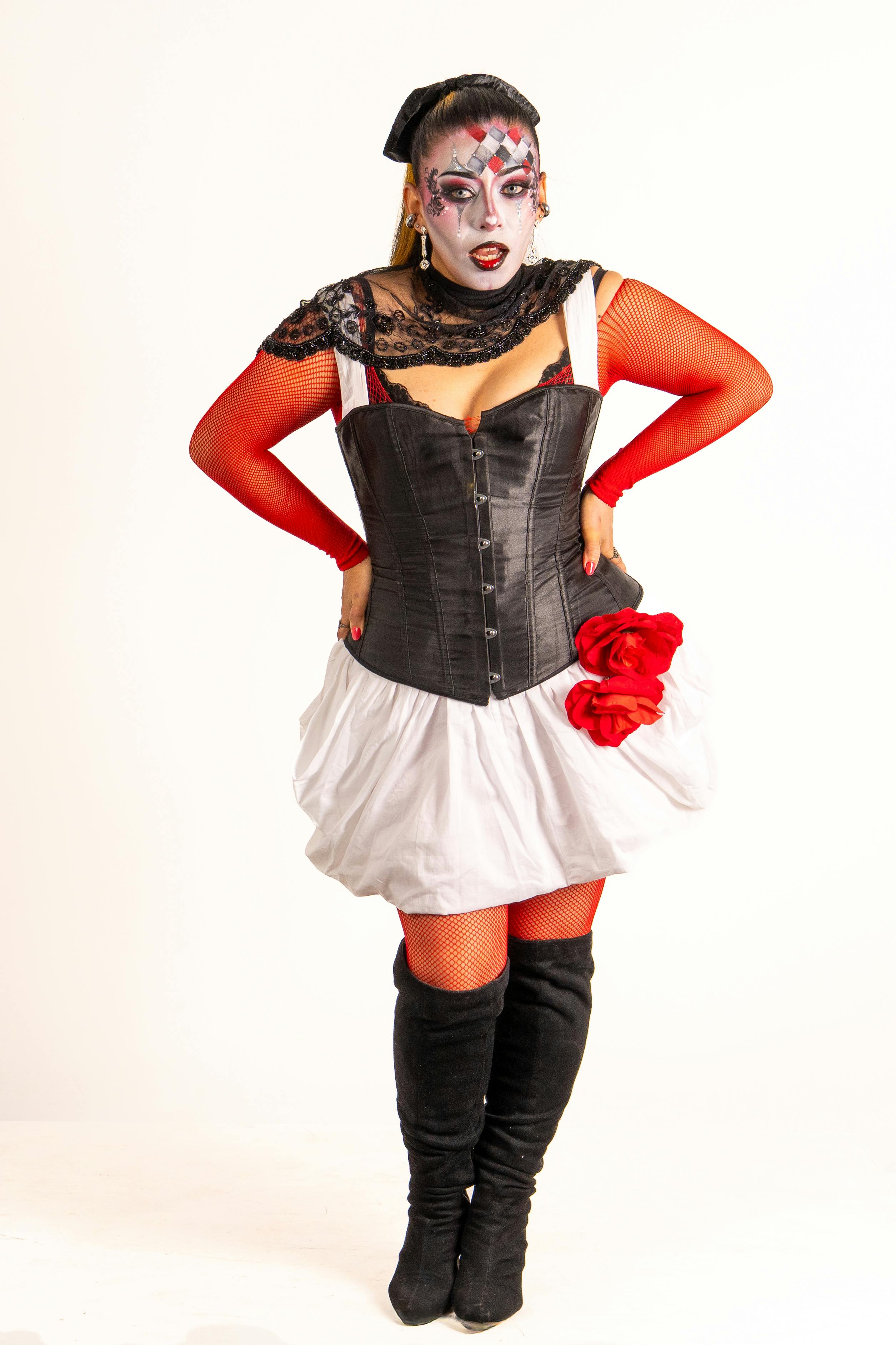 Gratis Una mujer vestida de arlequín negro y rojo con maquillaje de payaso creativo, posando con confianza. Foto de stock