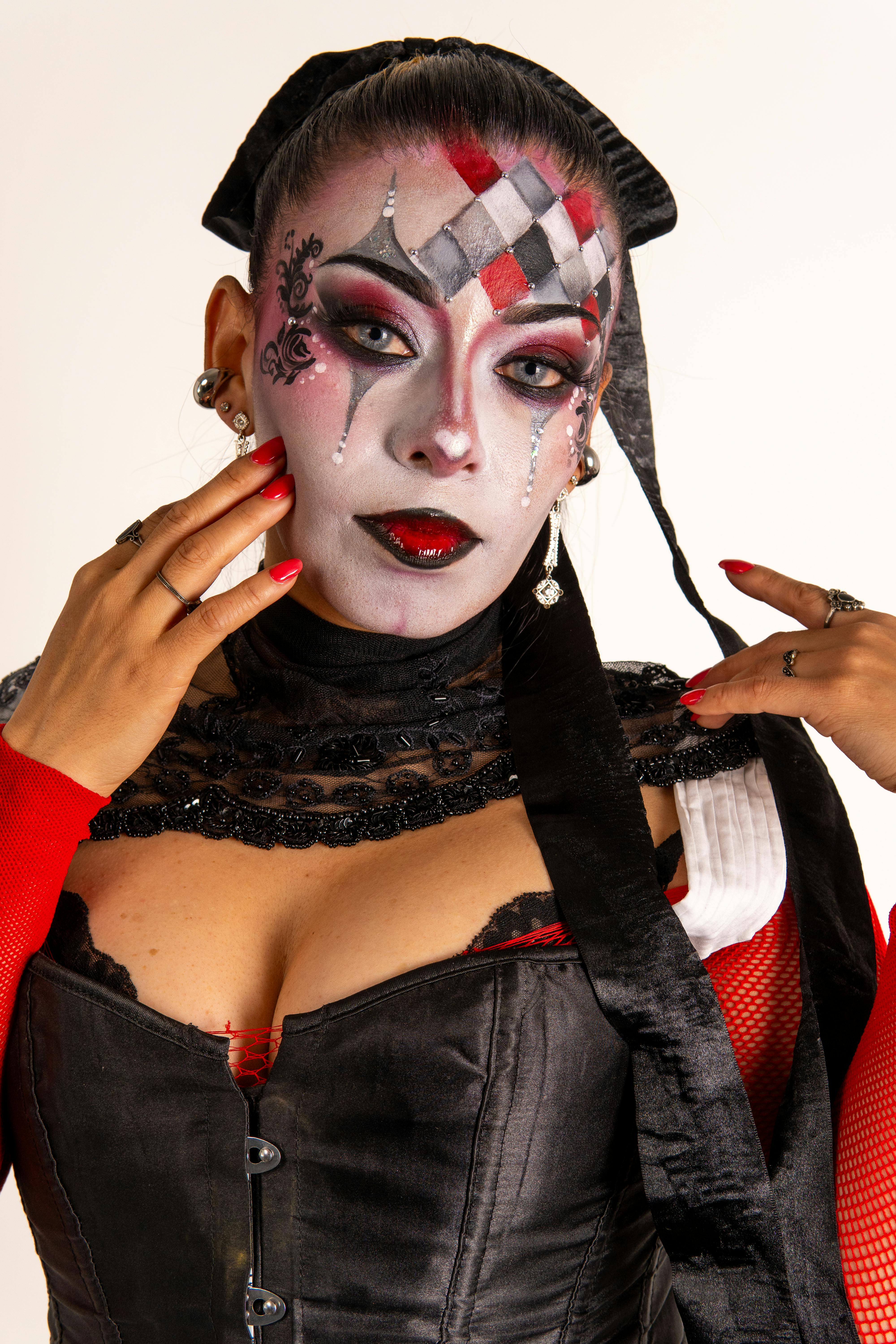 Δωρεάν Ένα Λατίνα μοντέλο επιδεικνύει πολύχρωμο μακιγιάζ αρλεκίνου με εντυπωσιακά κόκκινα και μαύρα ρούχα. Φωτογραφία από στοκ φωτογραφιών