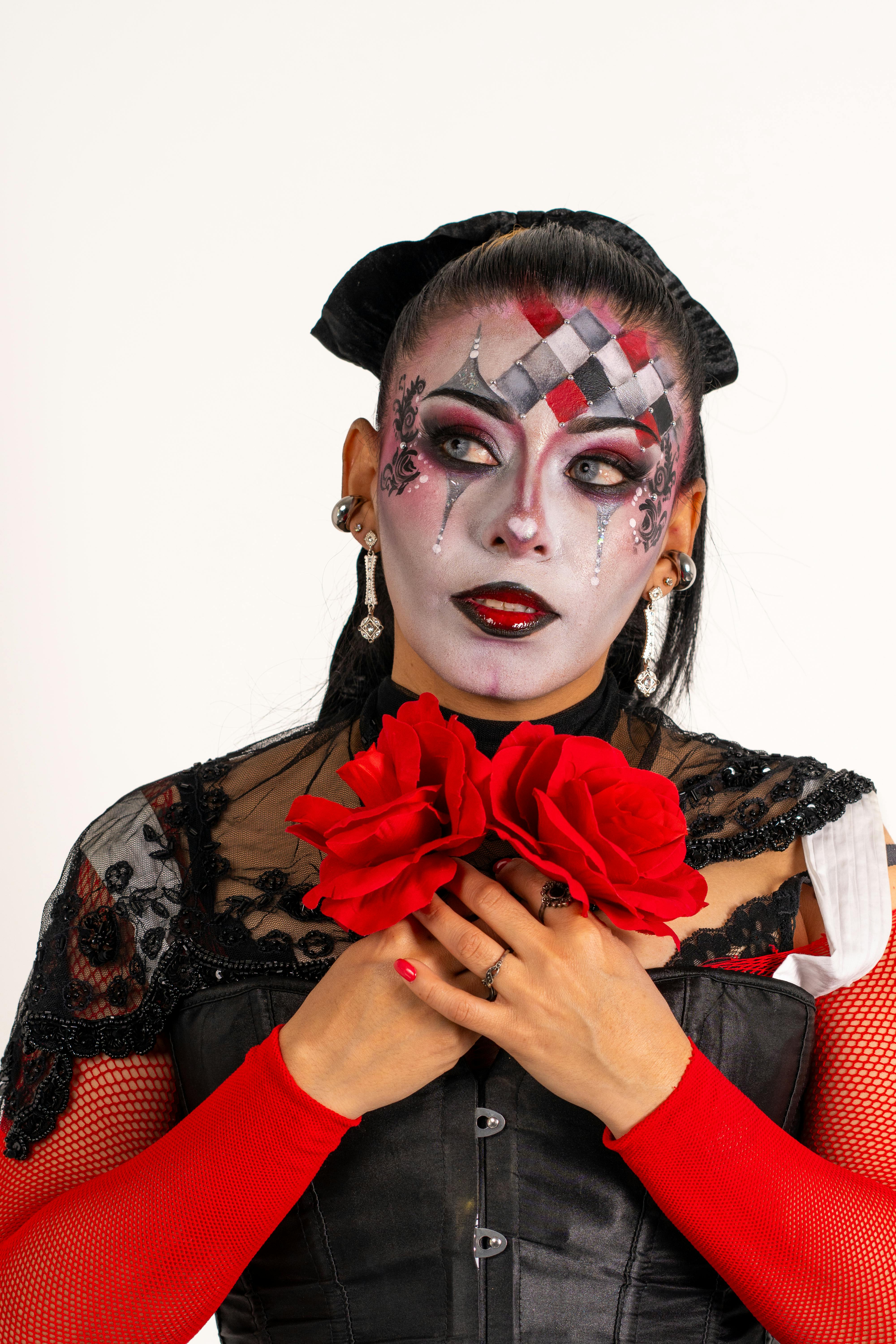 gratis Een Latijns-Amerikaanse vrouw met harlekijnclownschmink in haar hand, die rode rozen vasthoudt – een levendig en artistiek mode-statement. Stockfoto