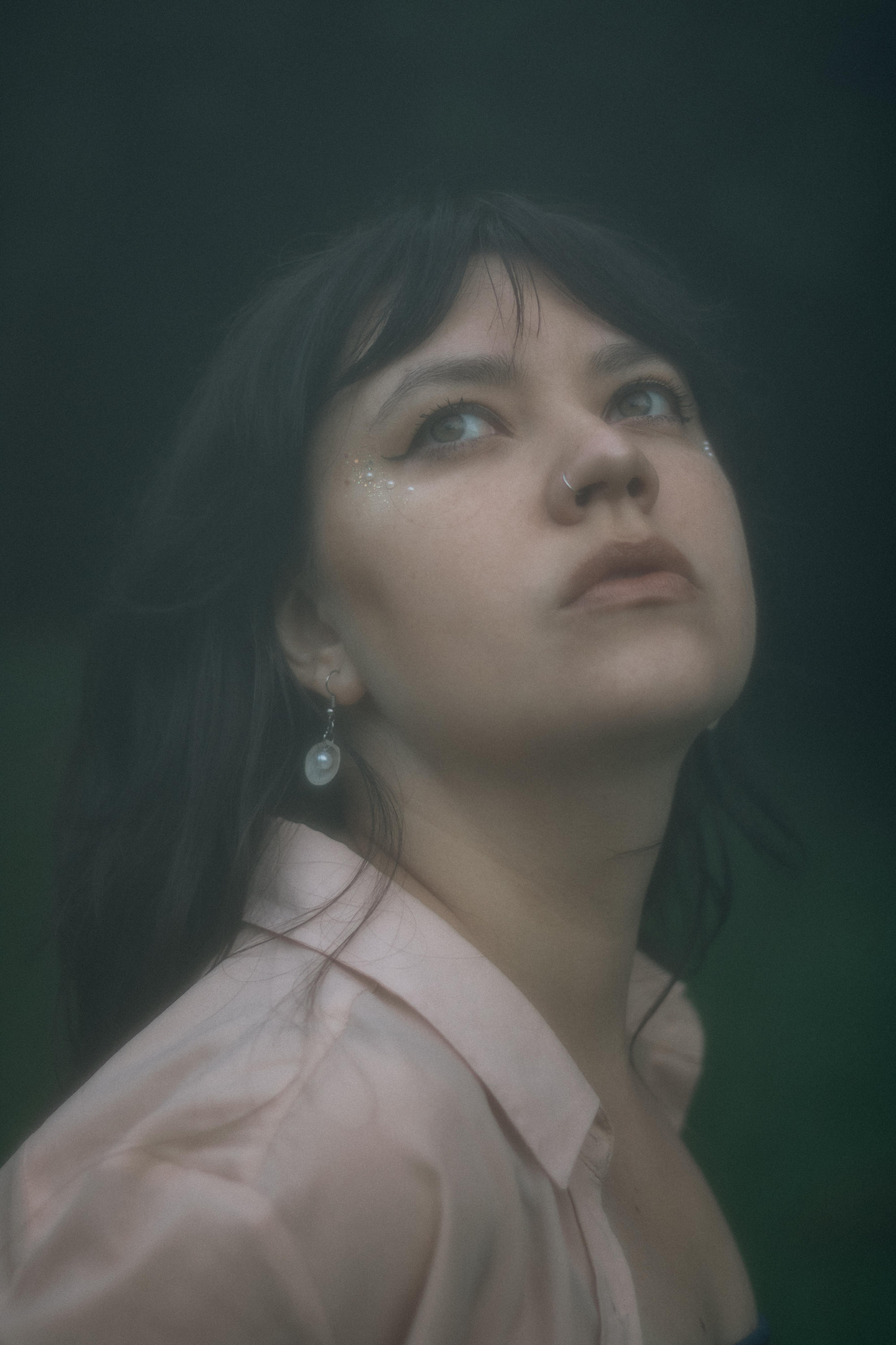 Gratis Ritratto malinconico di una donna che guarda in alto in un ambiente nebbioso, evocando un'atmosfera sognante. Foto a disposizione